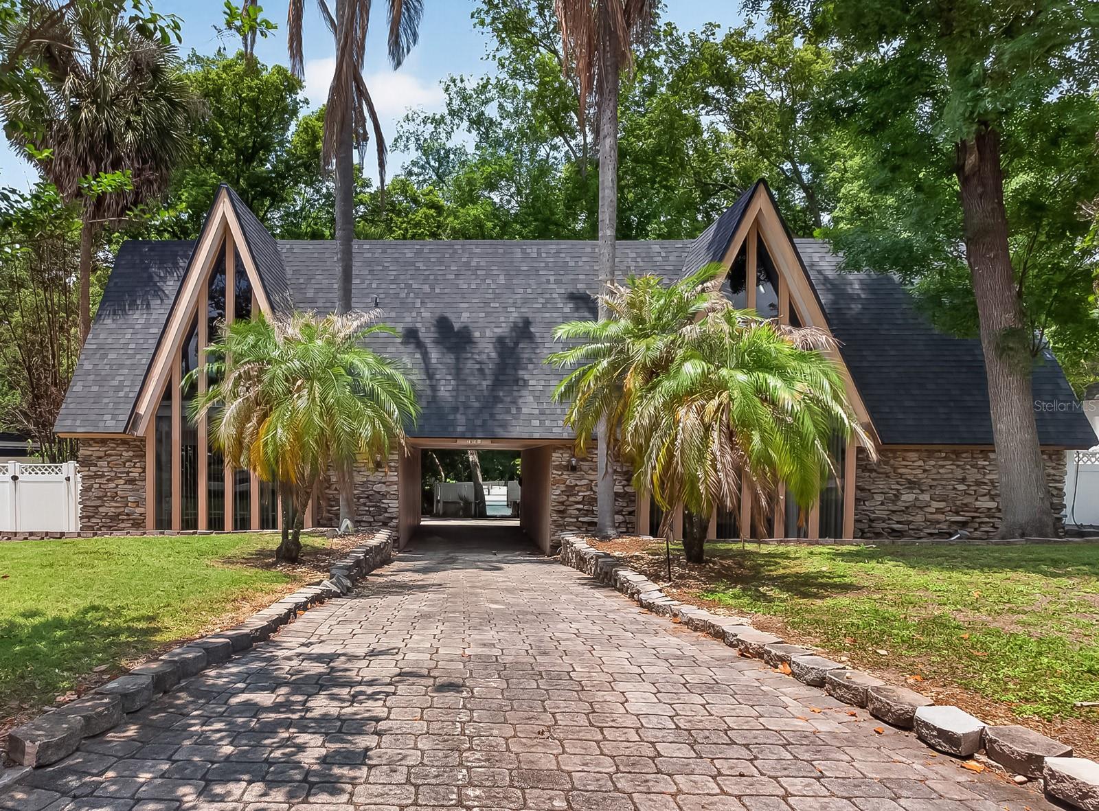 Virtually Staged. Located in one of Maitland’s established and tree-lined communities, this distinctive Mid-Century Inspired Chalet residence offers exceptional space, dramatic design elements, and endless potential for modern transformation. Positioned within sought-after school district  the home benefits from access to some of the area’s most well-regarded schools.The home’s impressive pavered approach sets the stage for its chalet-inspired architecture, where soaring A-frame rooflines, dramatic window walls, and natural stone detailing create an unforgettable presence beneath a canopy of mature trees — where “Colorado ski chalet meets Old Florida.”With 5 bedrooms and 3.5 bathrooms, the home is filled with high ceilings, expansive windows, and retro-inspired details that create character throughout. A striking open staircase with vintage styling showcases craftsmanship and design elements rarely found in today’s construction, while a massive paver courtyard welcomes guests and enhances the home’s unique indoor-outdoor lifestyle.Inside, the formal dining and sunken living room feature coffered ceilings and a dramatic circular brick fireplace centerpiece, while walls of windows flood the interiors with natural light. The spacious kitchen includes a cooking island, double wall ovens, closet pantry, breakfast nook, and an abundance of windows overlooking the private backyard area.Adding exceptional flexibility, the home also features a private in-law suite with its own separate entrance. The space includes a sleeping area, small seating/living space, private bathroom, kitchenette area with refrigerator and countertop workspace, and an eat-in area — ideal for multigenerational living, long-term guests, a private home office setup, or potential income-producing opportunities.The upstairs bedrooms open onto a rear balcony, creating a true retreat feel among the mature trees and landscaped surroundings.The primary bath features angular ceilings, oversized triangular windows, and a custom mosaic tile tub and double vanity that reflect the home’s original retro contemporary character.Outdoors, enjoy a sparkling swimming pool surrounded by shade trees, an expansive paver deck, and a fully fenced yard ideal for entertaining, gardening, or creating a private oasis.Recent updates include new roof 2024, along with a transferrable shingle warranty, both A/C HVAC units replaced 2019 and 2023, hot water heater was replaced in 2019, 2023 electrical work done, 2022 high end Samsung dishwasher installed, transferrable premium home appliance warranty expiring Feb 3 2027, gas-powered portable generator and underground utilities.  This home presents an exciting opportunity for buyers seeking architectural character and the chance to personalize a spacious residence with cosmetic updates including flooring, wall finishes, and modern design enhancements.Conveniently located near top-rated dining, shopping, parks, and major commuter routes, Maitland remains one of Central Florida’s most desirable established communities, known for its timeless charm, mature landscapes, and exceptional location.