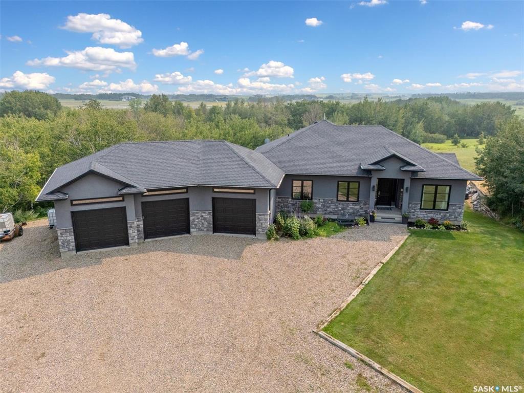 Welcome to 121 Valley Drive, just 10 minutes east of Saskatoon. This stunning 1,735 sqft walkout bungalow sits on 5.17 acres of beautifully manicured land with gently rolling hills and breathtaking southwestern prairie views. Built with exceptional quality and attention to detail, no expense was spared in constructing this remarkable home. The main level offers a grand foyer, open-concept living area with gas fireplace. The gourmet kitchen features full-height cabinetry, granite countertops, spacious dining area that leads to a sprawling covered deck—perfect for relaxing or entertaining, with multiple areas to gather and enjoy the scenery. With 5 beds and 3 baths, this home offers space and comfort for the whole family. The luxurious primary suite includes a spa-like ensuite with jetted tub, custom walk-in shower, double sinks, large walk-in closet. Two more bedrooms and a four-piece bathroom are also located on the main floor. There’s a dedicated main-floor laundry room and direct access to the oversized triple attached garage with in-floor heating and a wash bay—ideal for pets or gardening. The fully developed walkout basement offers two bedrooms, full bathroom, large family room, recreation/gym area, & stylish wet bar—ideal for entertaining friends and family. Additional features include in-floor heating throughout the basement/garage, built-in sound system with 4 audio zones, central air conditioning, central vacuum, 200-amp electrical service, 220V power in the garage, hot tub wiring on the lower patio, underground sprinklers, drip lines to dedicated tree areas, and high-speed fibre internet. Outdoor living is just as impressive, with a fruit orchard (apples, sour cherries, Haskap berries), raised garden beds, an in-ground PetSafe invisible fence, a skating rink area with fire pit. Note: highway #5 is being twinned and Drews Rd will have asphalt from the highway which ties into the current asphalt, so this property will be hard surfaced almost to the driveway.