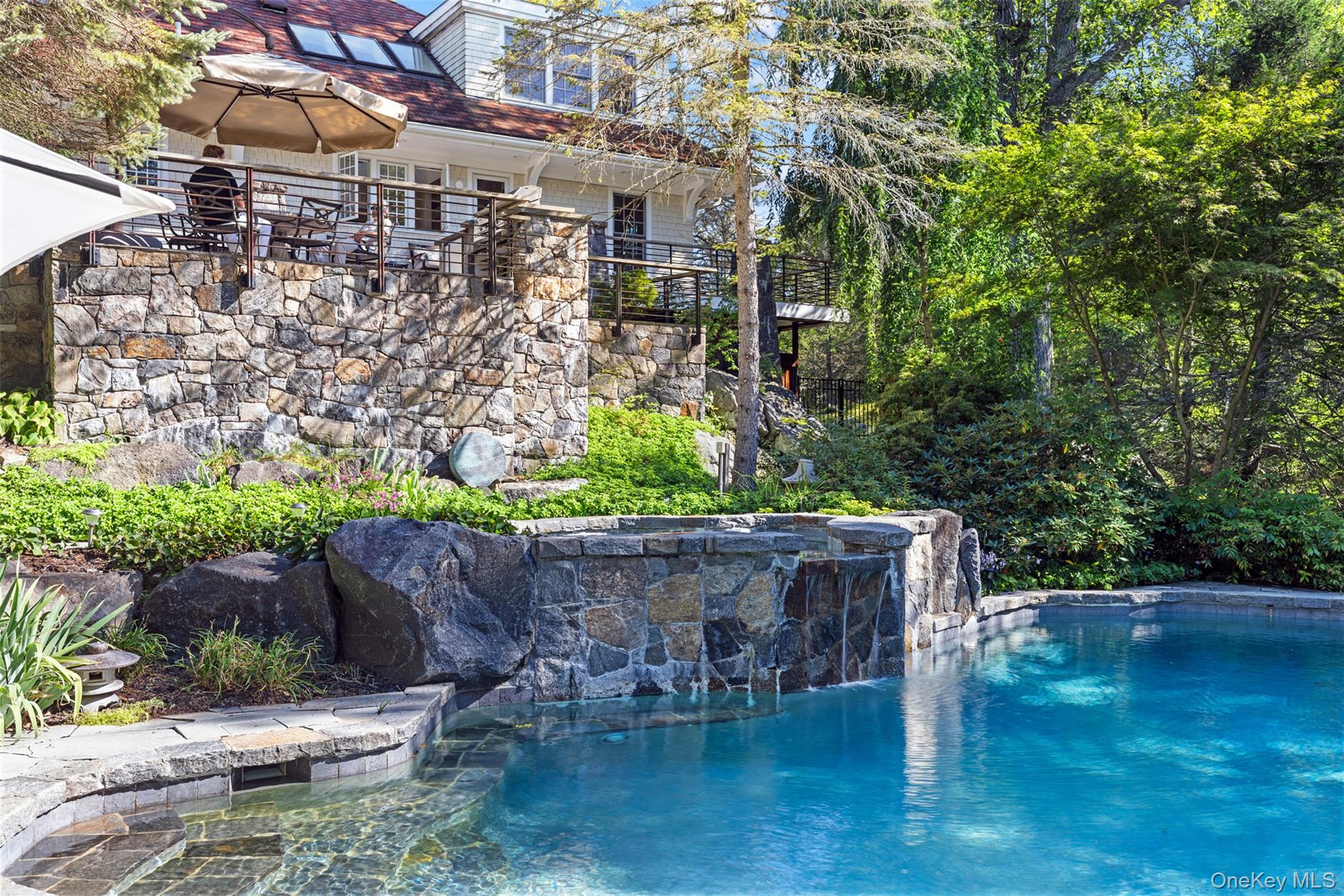 Generational Compound with all the luxuries & amenities one desires. Cascading pool with waterfall spa, guest house, pond, gardens and private property. Set down a quiet lane this resort-style estate is prime living-just one hour from NYC.  A tranquil place to call home for the discerning buyer who can spot special custom home. A thoughtful and tasteful full renovation was completed in 2013. The neo-classical post-and-beam design is a unique dwelling with no comparison in its stature and setting.

Situated high on a rock ledge with immaculate mature landscaping and ornate trees—from mighty Oaks and tall Hemlocks to Japanese Maples and Weeping Cherries—the property is a nature lover’s dream.

The property features a 3,500 sq ft main house with 3 bedrooms and 3.5 bathrooms, flexibility for a 4th bedroom in main house, and a 1,500 SF 1-bedroom, 1-bath guest cottage with a separate driveway.  Perfect for guests, staff living quarters, and/or rental income.

The main house features grand stone piers surrounding a large outdoor wrap-around deck with metal railing and Ipe wood, as well as a spacious stone patio overlooking a 13-foot-deep heated pool with spillover spa, all surrounded by stone. The stone patio includes a built-in stainless steel BBQ, also encased in stone, with an outdoor Viking refrigerator and built-in outdoor speakers for the pool area and patio.

Large stone steps lead to the patio and pool area, with a secluded wood walkway and level park-like lawn leading to the guest cottage. The pool area feels completely separate and extremely private, yet remains visible from the main house.

A large spring-fed pond is great for canoeing and kayaking, and the property includes lake rights to Lake Kitchawan, just a short walk down the private road.

The immaculate and well-maintained interior is anchored by a free-floating cantilevered staircase that serves all three floors of the home and becomes an artistic focal point of the house. It features a sunken living room with an open floor plan, plenty of natural light, a stone-faced wood-burning fireplace—French doors open to the wrap around porch and patio ideal for hosting guests and parties.

The main bedroom feels like a separate guest suite, part of the 2013 addition. This spacious room boasts 20-foot ceilings, pond views, marble bath and a walk-in closet.

A built-in music system is installed throughout most of the home, along with modern top-of-the-line appliances: Viking range, Miele dishwasher & Liebherr refrigerator. The kitchen features granite countertops and is flooded with natural light from three skylights and 20-foot ceilings.

Wood floors run throughout the house, with a marble-tiled floor in the front entrance.

The home is equipped with propane heat and central air, served by one 1,000-gallon buried tank with stone surround for the main house, and another 1,000-gallon buried tank for the guest cottage and pool/spa heat.

Additional features include an outdoor shower, steam shower in the third-floor bathroom, fire pit, fenced dog pen, shed, gravel driveways, well with water treatment system, gas fireplace with stone surround on the first floor. 

A wonderful retreat not to be missed.