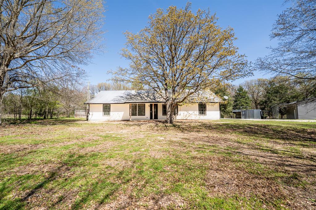 Private wooded 8.4 acres comes with a workshop and 3 bedroom, 2 bathroom house! A tree-lined drive brings you past a pipe-fenced entrance. You'll notice a front porch that is perfect for soaking under the shade of trees. Inside the vaulted living room, a stone fireplace with seating draws your attention in a cabin-flair interior. An open floor plan allows you to cook while entertaining guests or family. An extra large island with breakfast bar seating, granite countertops, stainless steel appliances, and access to the back porch compliment the kitchen. With a split bedroom layout, the primary ensuite includes a walk-in shower and garden jacuzzi tub. Additional bonuses are a new HVAC in 2022, new screws in roof in 2024, new septic pump in 2024, and recessed lights. A back porch provides a spot for grilling or watching the wildlife. The 30' x 40' workshop comes with concrete floors, 2 roll up doors, 10' x 10' roll-up door at the front and 9' x 8' roll-up door on the side, 1 walk-thru door, and a 10' x 40' covered lean-to area for equipment or vehicles. A shed could be used for a chicken coop, other farm animals or for more equipment storage. Make this wooded retreat your exclusive hideaway!