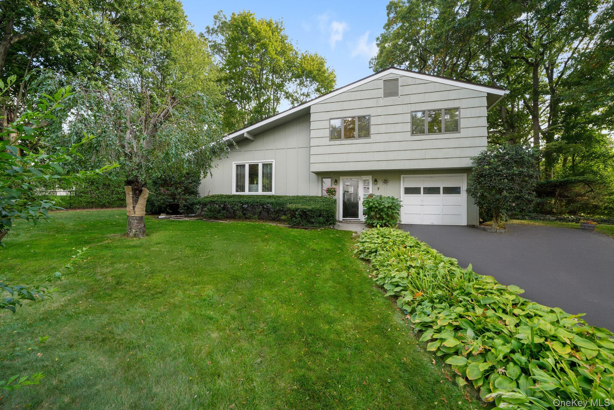 Welcome to this charming split-level home nestled at the end of a peaceful cul-de-sac on a beautifully level lot. This delightful three-bedroom, two-and-a-half-bathroom residence is the perfect place to call home.  Step through the sun-drenched entry foyer and discover a convenient home office featuring picture windows that flood the space with natural light. The upper level showcases a spacious living room with oversized windows and gleaming hardwood floors, flowing seamlessly into the formal dining room. Glass doors open onto a deck overlooking the private yard, creating an ideal indoor-outdoor connection. The eat-in kitchen provides easy access to the deck and yard, making entertaining effortless. Upstairs you will find two generously sized bedrooms that share an updated full bathroom, while the primary suite offers the luxury of a private bathroom retreat. The lower level houses a fantastic recreation room complete with a bar area, plus ample storage and utility space. Freshly painted - 7 Green Acres is ready for you to unpack you bags. The outdoor space truly shines with its level lot and deck perfect for relaxing or hosting gatherings. Centrally located, you'll enjoy convenient access to grocery shopping and public transportation, with the Hartsdale Railroad Station nearby for easy commuting. This well-maintained home combines comfortable living spaces with practical features, all situated in a quiet neighborhood setting that offers both tranquility and accessibility to everyday conveniences. A Must See!