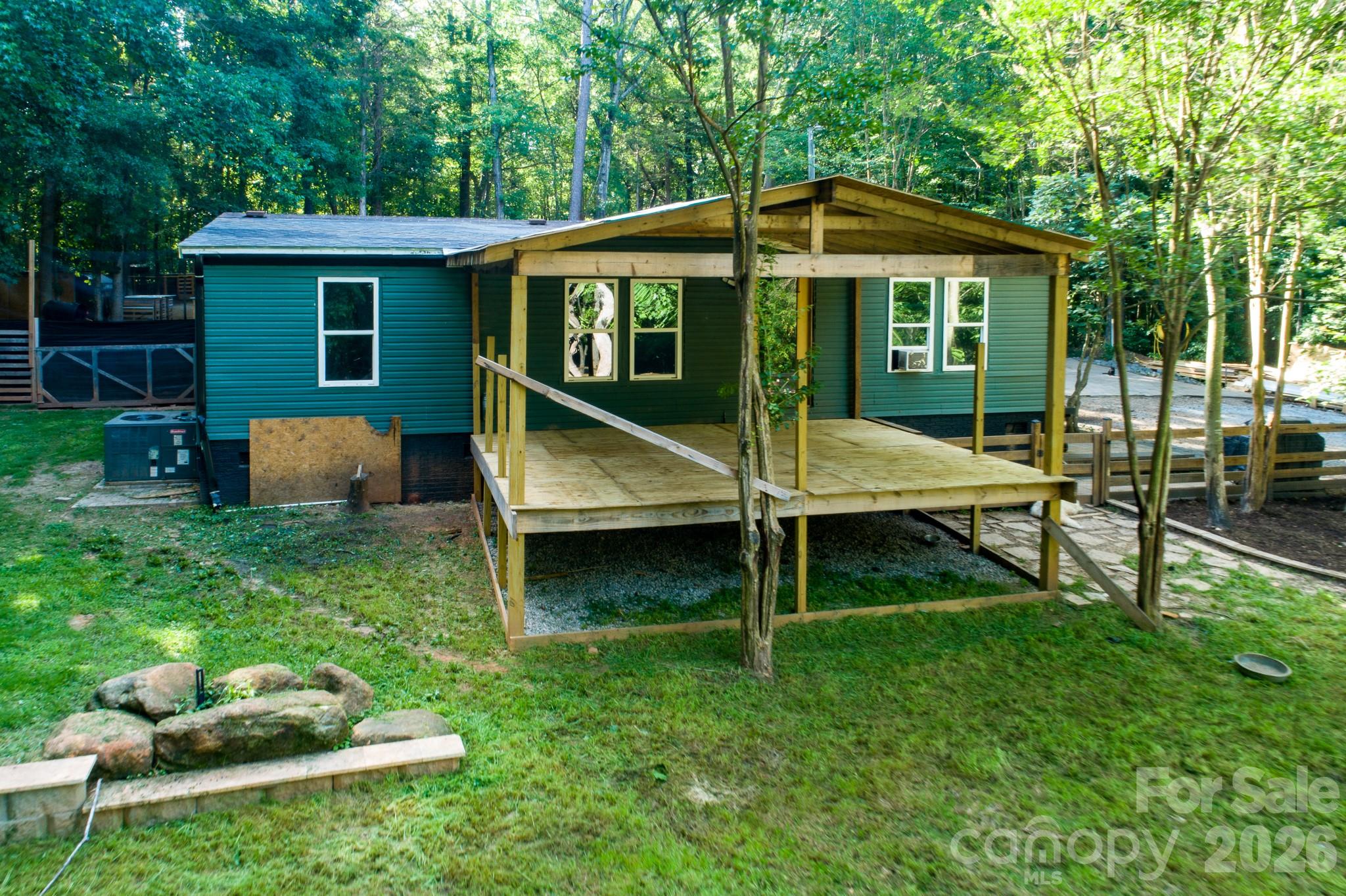 Welcome to 2268 Forest Music Drive, a private, wooded retreat offering approximately one acre of space and a unique mini-homestead setting. Surrounded by mature trees, this property provides plenty of room to enjoy the outdoors, with fenced areas, animal enclosures, storage structures, and a spacious covered porch/deck.Inside, the home features an open living, dining, and kitchen layout with updated LVP-style flooring and distinctive wood trim throughout. The kitchen offers granite countertops, abundant cabinetry, a full-height backsplash, modern range hood, black appliances, and a large center island with seating. The living area is spacious and comfortable, with direct access to the covered porch and peaceful wooded surroundings.Additional features include generously sized bedrooms, ample closet and storage space, an interior laundry area, and numerous updates throughout the home. One bathroom renovation remains unfinished, giving the next owner the opportunity to complete it to their own taste.This property is ideal for buyers seeking privacy, space for animals, gardening, hobbies, or a more self-sufficient lifestyle while remaining convenient to Clover and surrounding York County communities. The chicken coops and related animal enclosures are not included in the purchase price but may be negotiated separately if the buyer would like them to remain with the property. Property is served by community water and a septic system. Buyer and buyer’s agent to verify all information, permits, square footage, utility systems, and financing eligibility.