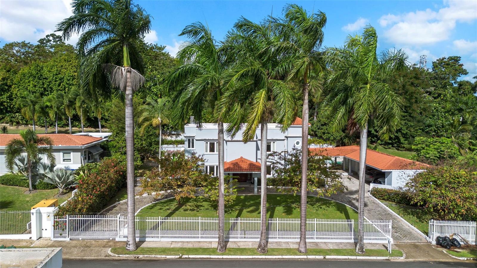 At 1858 Acacia Street, life slows down in the best possible way.This is the kind of home where childhood memories take root, where birthdays spill out into the garden, where Sunday mornings begin with sunlight filtering through the trees and end with laughter around the table. Set on a rare and beautifully flat 1,900m² lot in the heart of Santa María, this residence isn’t just a house, it’s a place to grow, gather, and build a life.The arrival alone feels special. A long, gently curving driveway lined with manicured lawns and mature palm trees creates a sense of calm and anticipation. Behind the gates, a green esplanade leads you to a covered entrance and a solid wooden door framed by custom wrought iron, an elegant welcome home, every single day.Inside, the space opens with grace and light. Double-height ceilings and a sweeping staircase set the tone, while marble floors ground the home in timeless elegance. The layout flows naturally, allowing daily life and special moments to coexist with ease. Formal living and dining areas are perfect for celebrations and holidays, while the family room invites movie nights, homework afternoons, and unplanned conversations that stretch late into the evening.Just beyond, the heart of the home continues into a generous kitchen overlooking the backyard and pool, where meals are prepared with the windows open and you can enjoy the green landscape. A thoughtfully designed bar area nearby makes hosting effortless, whether it’s a casual gathering with friends or a quiet glass of wine once the house settles for the night. A private library or office offers a peaceful retreat for work, reading, or reflection. Upstairs and tucked away, four (4) ensuite bedrooms provide comfort and privacy for every member of the family. High ceilings and tranquil views of the surrounding greenery create restful spaces designed for growing years.Whether you have a growing family, frequent guests, or a love for cars, this home is ready to accommodate it all. A covered garage for three vehicles and ample on-site parking ensure everyone, and everything, has a place. Peace of mind and space to spare, right at home.And then there’s the outdoors, the true soul of this property. The expansive backyard feels like a private park, surrounded by mature trees and lush landscaping. The pool sits at the center, framed by flowering trinitarias and carved stone fountains that bring a gentle, resort-like calm. With so much open green space, there’s room to dream bigger; perhaps a pickle ball court, a playground, garden paths, or future additions tailored to your family’s evolving lifestyle. Set on one of Santa María’s quietest and most desirable streets, with virtually no traffic, this home offers something increasingly rare: privacy, space, and a sense of belonging. It’s where you can roam freely, neighbors feel like friends, and every day ends with the comfort of knowing you’re exactly where you’re meant to be.This is not just where you live.This is where your family’s story continues.