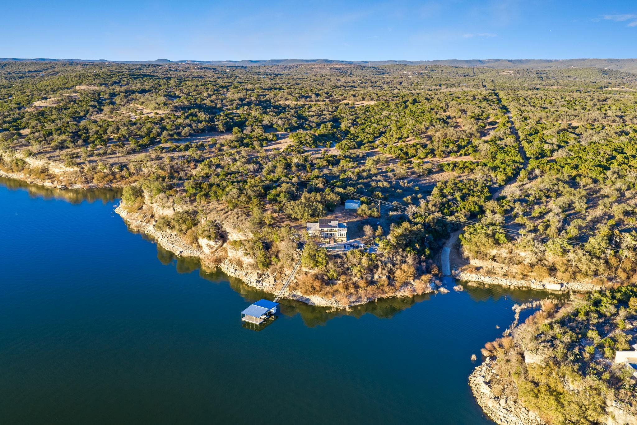 Private waterfront retreat spanning 70 acres with 1,200 feet of deep-water frontage on Lake Travis - an increasingly rare offering defined by scale, privacy, and enduring quality. Elevated above the shoreline, the estate captures sweeping panoramic views of the lake and Texas Hill Country.  The north-south facing custom residence was designed for efficiency and comfort, featuring a standing-seam metal roof and significant infrastructure upgrades that support long-term performance and reduced utility costs, including a geothermal heat pump, tankless water heaters, solar panels, and a backup battery system.  Outdoor living is a defining highlight. A heated pool overlooks the water, while a meandering path leads to a fire pit gathering area and a private dock accessed by tram. The dock includes two boat slips, two jet ski slips, and additional storage. Bookended by two protected coves, the property offers an estimated 1,400 feet of total frontage and is grandfathered with riparian rights on Lake Travis.  Additional improvements include a covered pole barn with RV hookups, a 900-square-foot workshop with 220V outlets, fruit trees, and a dedicated garden. Divided into two parcels, including 60 unrestricted acres, the property carries a wildlife exemption for potential tax advantages.  With expansive acreage, significant waterfront access, a boat ramp, and flexible zoning, the estate offers compelling future potential. Buyer to verify taxes, square footage and approvals.