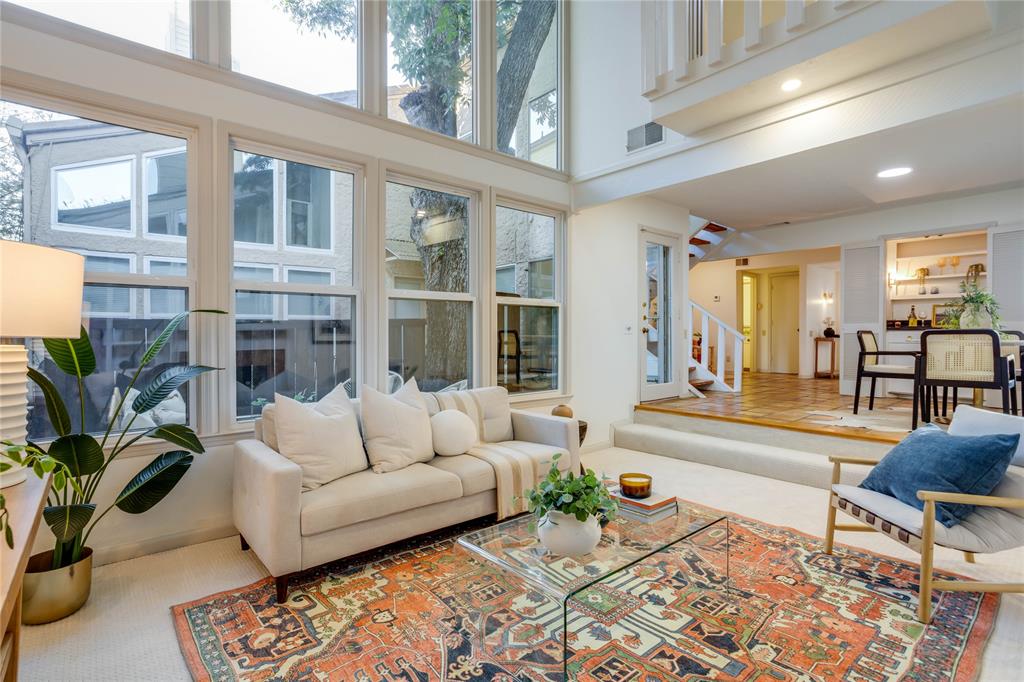 Some homes are built around a kitchen or a view. This Oak Lawn townhome was built around a single mature tree, and two stories of windows make sure you never lose sight of it. This is 1970s design at its most livable, and the recent renovation treated it that way, repairing and refreshing the house while keeping the period details that give it identity. The entry opens onto warm Saltillo tile and a stair of open wood treads. In the living room, the windows frame the courtyard’s trunk and canopy, so the room moves from green morning shade to a softer gold by evening. A Saltillo tile fireplace and built-in shelving anchor the space, while the dining area sits steps up, close enough for conversation to carry. Louvered doors conceal a wet bar. The galley kitchen is clean and well organized, with subway tile, lit glass shelving, and stainless appliances. At the far end, three tall windows set the breakfast nook in daylight, with direct access to the attached two-car garage. Upstairs, the primary bedroom stretches 20 feet beneath a towering vaulted ceiling, with two closets and sliding doors to a balcony finished with a new wood and metal rail. Its bath pairs a newly built shower, soft blue vertical tile behind a custom glass panel, with an onyx-toned vanity kept on purpose. The second bedroom is the surprise: bifold panels open to a Juliet balcony above the living room, and it has an exterior balcony of its own. Guest room, office, reading loft. It adapts. A retiled hall bath and a true laundry room complete the level. That restraint runs through the house. The avocado powder room sink and the cobalt laundry counter stayed, while fresh paint, new carpet, and newly tiled baths brought everything around them current. The result feels restored rather than remodeled. Beyond the courtyard wall, Oak Lawn fills in the rest. Cedar Springs dining, the Katy Trail, and the downtown skyline are minutes away, close enough to join, easy to leave behind once the tree is back in view.