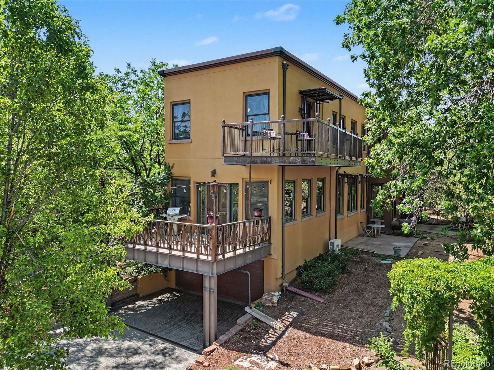 Set on a quiet street in the sought-after Applewood / Linda Vista neighborhood, this home offers mountain views amid mature landscaping — a rare achievement in custom design where Old World Tuscan craftsmanship meets the ease of modern American living. A stamped Belgian-style driveway with flagstone accent, marked by a striking large-scale metal "Arch" at the street entry, sets the tone on arrival, while wood-frame windows, solid wood interior doors, and hand-forged ironwork echo the European villas that inspired this home. Copper trim throughout the interior and exterior reflects a level of artistry seldom found in Colorado.The living room anchors the home with soaring windows and a gas fireplace. The kitchen is a chef's retreat with a custom copper sink and slab marble counters. A two-story study with floor-to-ceiling built-ins and a library ladder offers a rare architectural statement, open to the walkway above.The upper level was built for how families live: bedroom-level laundry, a family room on the same floor, and a primary suite with a soaking tub, private deck access, and uninterrupted Flatirons views. Both upper baths feature double vanities; guest bedrooms share their own covered deck.Outside, the grounds are equally enchanting — a treehouse, a goldfish pond, garden-ready beds, and a vine-covered swinging seat. A commercial-grade TPO roof with heated seams and a full climate system (boiler, forced-air furnace, evaporative cooling, and a split system in the primary suite) ensure year-round comfort. Four garage spaces plus abundant storage in the detached garage and basement.Directly across from Graham Park's open space, this is a peaceful sanctuary with unmatched character. Horse zoning potential — buyers to verify with Lakewood. Buyers to verify all measurements and information.1955 home scraped, 2001 current build, updates 2014 and 2016 or newer.