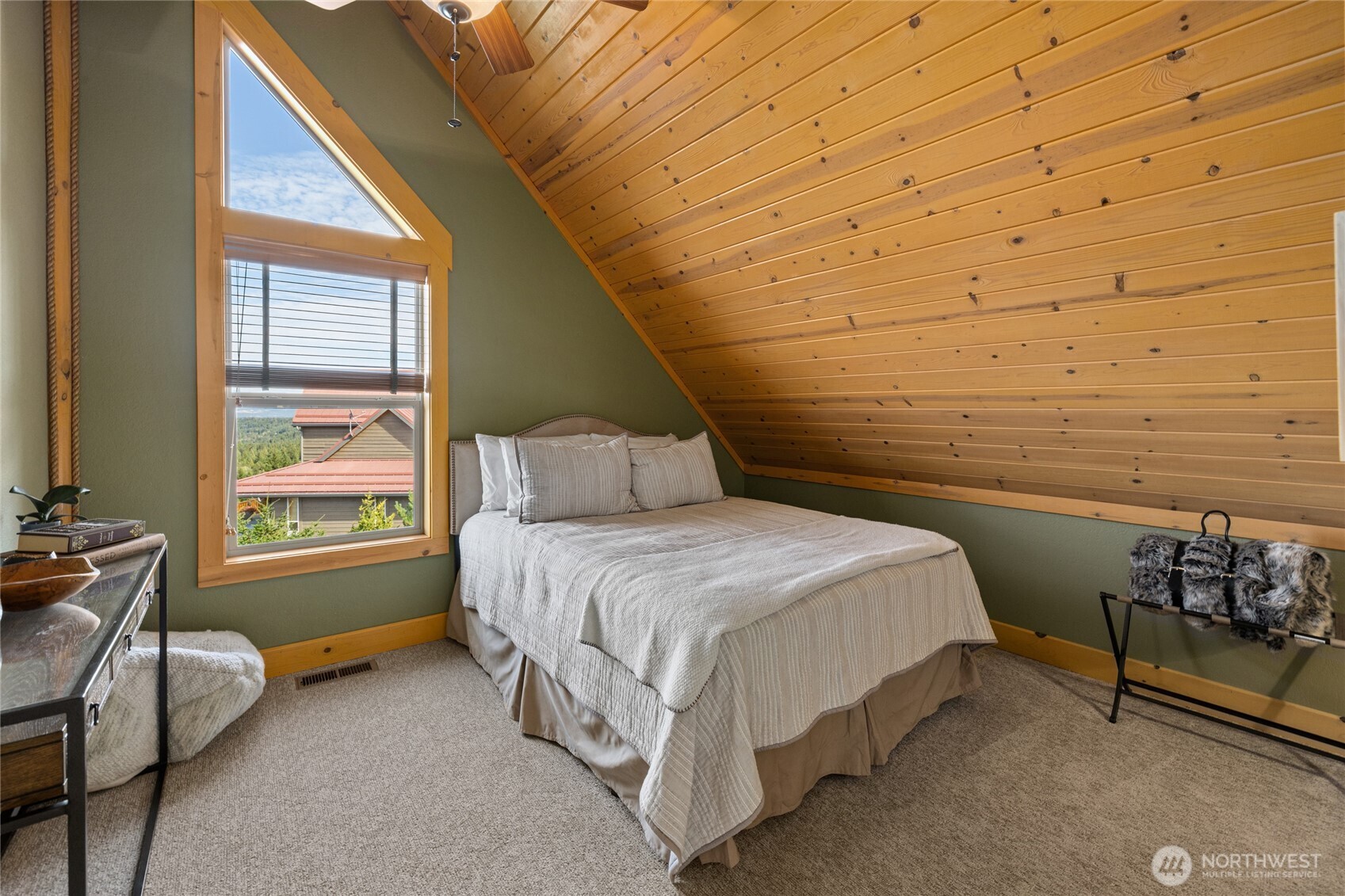 Additional guest bedroom with vaulted wood ceiling, large window, and warm mountain-home character.