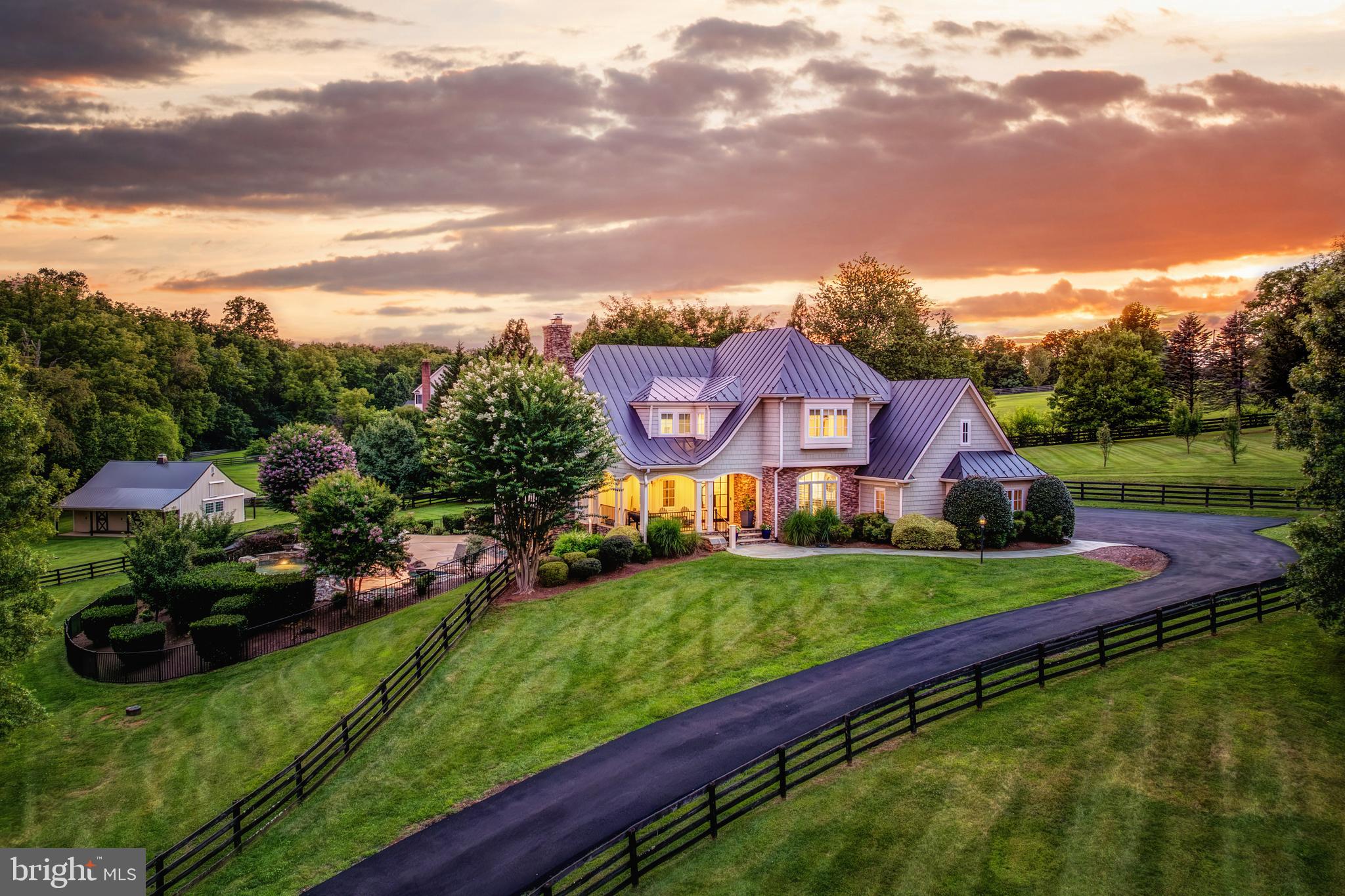 Welcome to Skyfall, a custom-built modern farmhouse thoughtfully designed with the finest materials, exuding sophisticated luxury on 9.08 meticulously fenced acres secured by private electric-gate access. Nestled on prestigious Peale Lane—a secluded enclave celebrated for estate-quality homes amid Loudoun County’s picturesque wine country—Skyfall offers exceptional privacy, yet is mere minutes from vibrant downtown Leesburg. Crafted with impeccable attention to detail, the home's striking entry features imported black French steel doors beneath a dazzling Schonbek German crystal chandelier, accented by tray ceilings and crown molding throughout the main level. Durable Hardi-plank siding, a sleek full metal roof, newly paved driveway, and new Carrier HVAC systems with UV technology underscore the superior quality of construction. The luxurious main-level primary suite includes dual walk-in closets, French steel doors, and a cozy sitting area with a Jotul wood stove surrounded by marble. Its opulent ensuite bath features reclaimed barn doors, cathedral-arched windows, an oversized Kohler soaking tub, Toto Japanese toilet, dual Indian marble vanities, and frameless rainfall shower. Two chic powder rooms—including one concealed within the laundry—ensure convenience. Ascend the dramatic waterfall staircase to three spacious bedrooms, each with generous walk-in closets. One bedroom has a private ensuite bath with marble vanity; the other two share a Jack-and-Jill bathroom with dual Carrera marble vanities, clawfoot tub, and seamless glass shower. A charming reading nook completes the upper level. The gourmet kitchen impresses with expansive floor-to-ceiling cabinetry, waterfall quartz island with cabinetry on both sides and integrated power, WiFi-enabled Thermador appliances including discreetly integrated fridge, freezer, dishwasher, wine fridge,  6-burner range with griddle, twin ovens and integrated Chef's hood.. Under-cabinet lighting, hidden outlets, and a trough sink with dual faucets enhance functionality. An adjacent hidden pantry mirrors kitchen finishes with quartz counters and open English oak shelves, and handmade hickory barn door entrance. The expansive family room features soaring cathedral ceilings, exposed wood beams, rustic stone fireplace insert, built-in English oak workspace, and access to the wraparound porch. A formal dining room, illuminated by a statement fixture, is perfect for entertaining. The finished lower level is an entertainer’s paradise, highlighted by a reclaimed Virginia barn wood bar with Indian marble, dishwasher, EuroCave wine fridges, beer fridge, and sink. A stacked stone fireplace with Jotul stove warms the rec room, while a hidden theater/music room lies behind a custom bookcase. A guest suite with reclaimed wood vanity and full bath, fitness room, workshop, and ample storage offer additional comfort, all with direct access to the pool deck. The outdoor haven centers around a stunning 30,000-gallon PebbleTech gunite pool, tanning ledge, 8–10-person spa, and impressive 11.5-ft deep end, that slopes to a swallower end.. Exterior amenities include a Trex deck, flagstone patio with Jotul fire pit, and stone-enhanced pool deck. Custom artisan electric gates by Aurora Services on Virginia bluestone columns feature AES PRO smart-device control. Equestrian facilities include a pristine 4-stall barn with new metal roof, hot/cold water, tack room, hayloft, and adjoining 7-acre fenced paddock. Facing nearly due south, Skyfall feels secluded and serene yet is conveniently situated only minutes from Dulles Airport and within easy driving distance of Washington, DC. Located just 4.6 miles from historic Leesburg with quick access to Route 15, the Greenway, over 50 wineries and breweries, and scenic trails including the Appalachian Trail, Skyfall represents a rare opportunity to experience refined craftsmanship and luxurious comfort in Northern Virginia’s most desirable countryside setting.