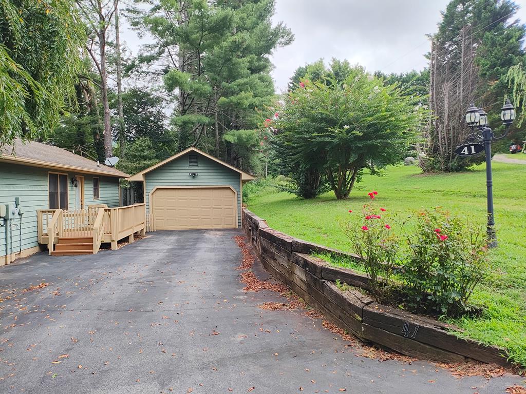 Idyllic setting for this charming 2 bedroom/2 bath home (split bedroom plan) with gorgeous hardwood flooring and tile throughout. Open floor plan with a vaulted ceiling and beam in the living area. Floor to ceiling stone gas/wood fireplace and French door access to the front, screened deck to enjoy the peaceful view. The dining area has wood corner shelves, a wood shelf valance a bronze chandelier and a year round mountain view. The spacious kitchen has a tile floor and back splash with plenty of storage.  Beautiful white wood cabinets/drawers, a handy appliance garage, a slide out cutting board and stainless steel appliances with a new (2024) dishwasher. The laundry area, with a cute barn door is in the kitchen and has shelves for laundry/pantry items.  Directly off of the kitchen is the sizable guest bedroom with its own private bathroom, which has a wood vanity, a combo shower/tub and a view of the fenced in garden. French doors allow access to the open deck with a lovely view of the front yard.  The primary suite (off of the living area) includes a large bedroom with French door access to an open deck and the scenic views of the front yard and a side window as well.The bathroom has a wood vanity with a granite countertop, a combo shower/tub and even a window with a view! The latticed area under the deck provides ample storage.  Cute, fenced in side garden area where the new (2023) a/c unit is located and also access to the crawl space, which was completely encapsulated in 2024 and has a whole house water filter and a dehumidifier.  Front yard has a park-like setting with majestic, towering trees and a fire pit to enjoy family time together, or have coffee on the back deck and enjoy the mountain view. Paved parking/detached garage.  Fiber optic internet is available. Close to Lake Chatuge, Jack Rabbit Trail and Eagle Fork Vineyards.  Short drive to restaurants, grocery shopping and gas stations in Hayesville. Must see to appreciate. Schedule a showing TODAY!