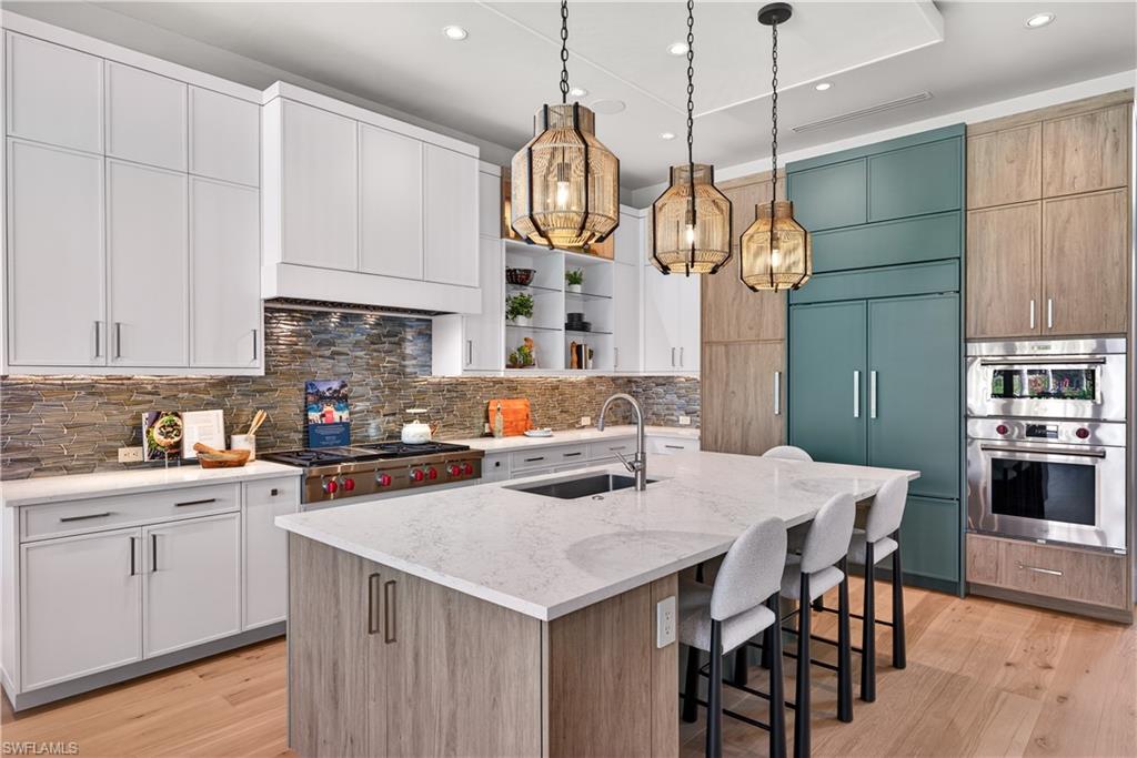 Kitchen featuring dual tone cabinets, a kitchen island with sink, light stone countertops, a kitchen bar, and pendant lighting