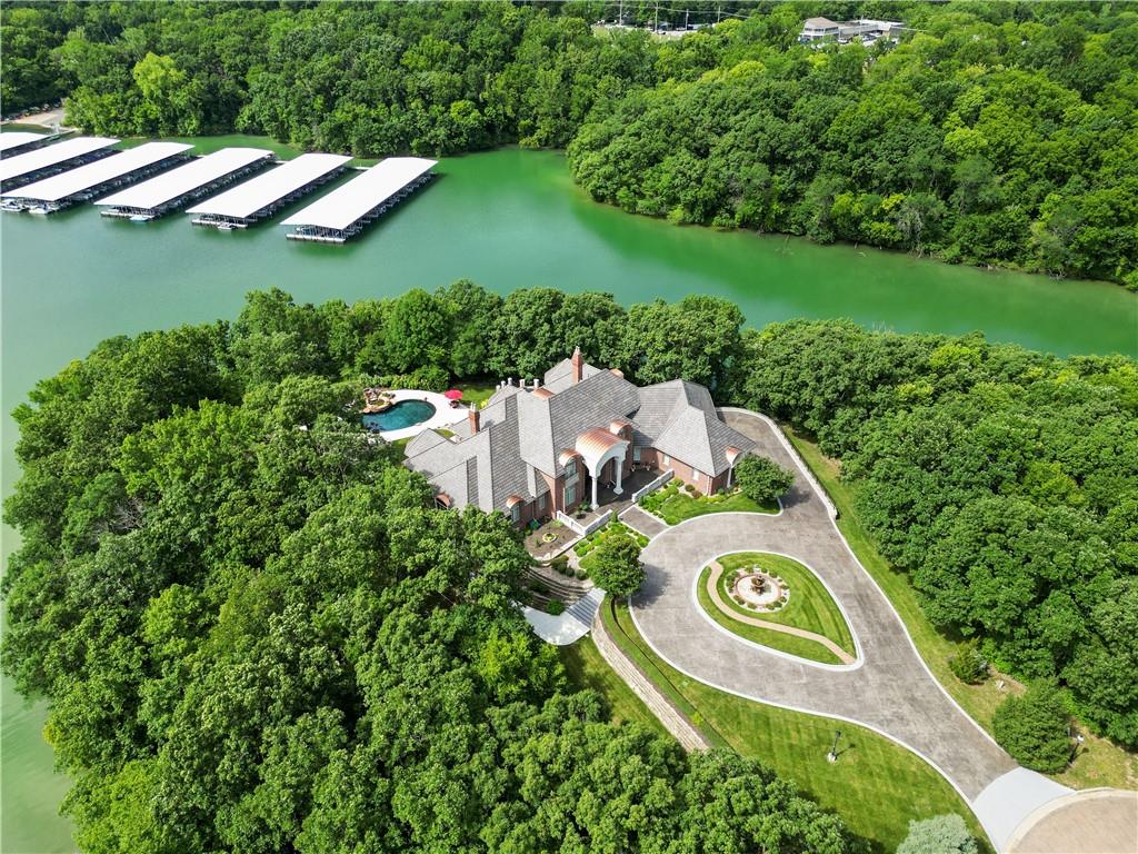 Situated on a private point in the West Shore of Riss Lake, this elegant lakefront residence spans 11,700 sq. ft. on 1.22 acres of beautifully maintained wooded landscape. Nestled within a private gated community, you'll be immediately impressed by the stunning exterior, impeccable circular drive, and custom glass entry. Inside, this meticulously designed home impresses at every turn. From the incredible custom stainless steel and glass staircase to the expansive entertainment area, this home is truly one-of-a-kind. Flooded with natural light, it boasts soaring ceilings and walls of windows. On the main level, you'll find a formal living and dining room, a large office, a separate den, a cozy hearth room, a designer kitchen with Viking and Sub Zero appliances, and a beautiful sunroom with incredible views. The Owner's suite is a retreat filled with special details such as custom ceiling features, a lovely sitting room, expansive closets, a whirlpool tub, and more. The upstairs features a large loft area and three spacious bedrooms, each with private baths and walk-in closets. This home also includes a large gym, a playroom, and a fabulous home theater. 
For hosting, there’s a full bar and a second kitchen, making entertaining guests an effortless yet elevated experience. Step outside to your own resort-like oasis, featuring a beautiful lagoon-style pool, an outdoor kitchen, and an expansive deck area to entertain or relax and enjoy the lake views. Just off the pool area is an indoor spa room with an attached bathroom and steam shower. The property includes a five-car garage ideal for car enthusiasts, plus a dedicated shop area. Don't miss this rare opportunity to own this masterpiece of craftsmanship located just minutes from MCI Airport, Charles B. Wheeler Airport, downtown KC, and the Plaza. Privacy, luxury, and location at their finest!  Taxes and square footage are estimated and should be verified by Buyer's agent.