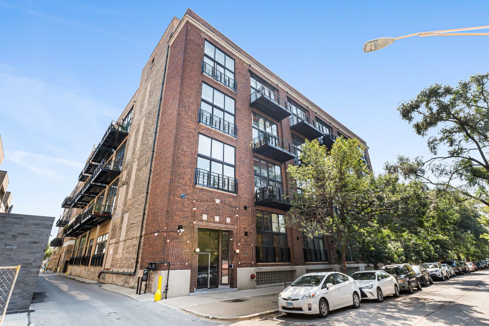 Set inside the historic Silk Factory Lofts, a four-story industrial conversion in Logan Square built in 1918, this top-floor 2-bedroom, 1-bath condo-loft pairs double height 20-foot ceilings with deeded garage parking and a 2023 mechanical overhaul. Floor-to-ceiling sliding glass doors with automated shades frame the west-facing living area, overlooking the lush treeline toward breathtaking sunsets, and exposed brick and a wood-beamed ceiling run the full height of the great room. The private balcony opens off the living room, in addition to the building's shared rooftop deck that delivers skyline views. All building balconies were refurbished in 2024 and 2025. The kitchen anchors the great room with a granite-topped island, wood cabinetry, and a GE appliance package, while a built-in dry bar off the living area holds a Criterion wine refrigerator. Oak hardwood floors run through the living, dining, and kitchen spaces, with wood-laminate floors in both bedrooms. The primary bedroom hides behind the privacy of a sliding reclaimed barn door, and double closets line the space within. The bath offers a double-sink vanity with composite countertops. In-unit GE laundry is included, and the climate control unit was installed new in 2023 by ABC Heating, Plumbing & Air. A deeded, heated & cooled garage parking space, oversized enough for additional storage, is included, along with a separate storage locker in the basement. In addition to the shared rooftop terrace, residents also enjoy a lobby elevator and a freight elevator, a bike room, a video entry system, and USPS mailboxes/package delivery located inside the secure lobby. Steps from Humboldt Park and two blocks from the Bloomingdale Trail on The 606, the building sits a seven-minute walk from the CTA Blue Line at both California and Western, with Aldi and Jewel-Osco on Milwaukee Avenue close by for everyday errands, and hot Logan restaurants including Table Donkey and Stick, Osteria Langhe, the new Small Cheval Freeze location, Middlebrow, Solemn Oath Brewery, Gretel, and Parsons are steps from the front door. This Logan Square address puts the trail, the nightspots, the park, and the train all within easy reach.