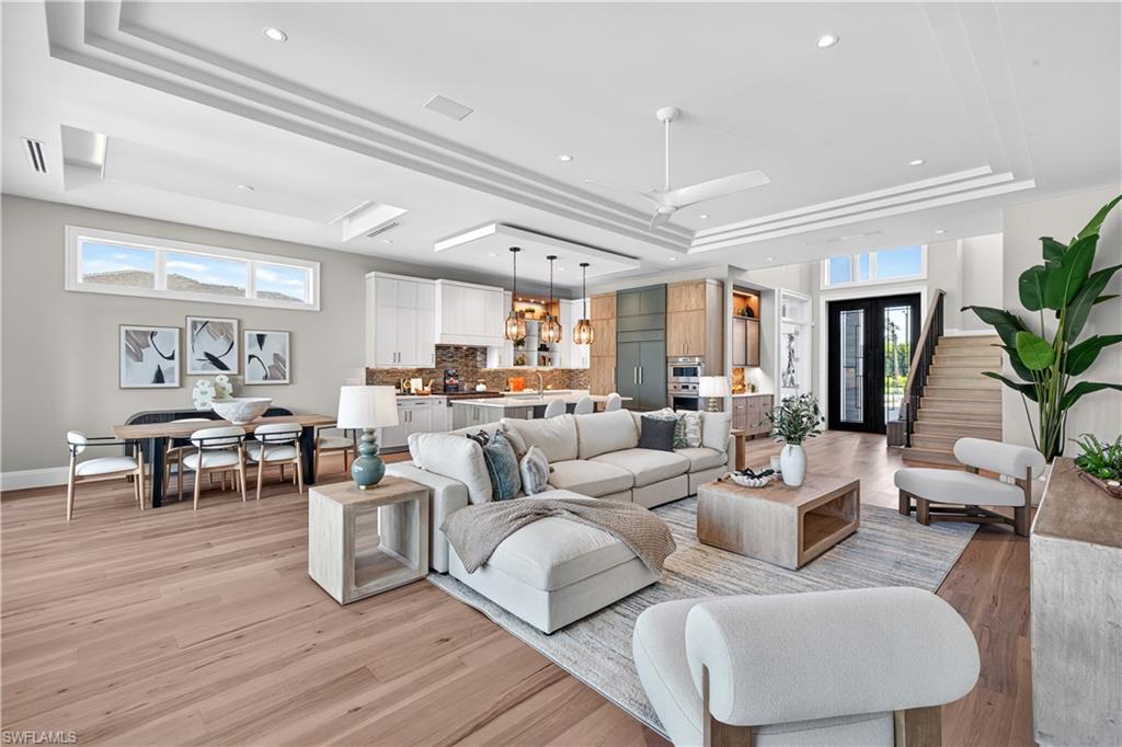 Living area with light wood-type flooring, plenty of natural light, a tray ceiling, a ceiling fan, and recessed lighting