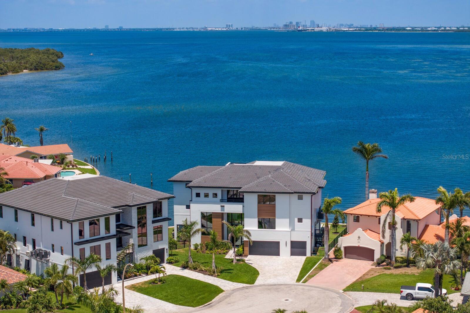 Recently completed to the highest standards, this stunning new construction Venetian Isles waterfront residence blends refined luxury with cutting-edge engineering. Built on pilings and reinforced with rebar/concrete, this elevated home offers unmatched strength, stability, and peace of mind. Poised gracefully at the edge of Tampa Bay, enjoy sweeping, uninterrupted views that extend across the glistening water to the skyline of St. Petersburg. Built by Tide Homes, a professionally designed interior provides a sophisticated aesthetic and curated elegance. From the moment you step inside, you’re welcomed by warm Chesapeake hardwood floors and a serene palette of premium finishes. The expansive main living area delivers sweeping floor-to-ceiling water views and a dramatic gas fireplace and feature wall which integrates a glass-enclosed wine cellar that anchors the formal dining area. A sleek chef’s kitchen is crafted with carbon-neutral Dekton countertops and backsplash, Thermador and Bosch appliances, a butler’s pantry/full prep kitchen with additional dishwasher and refrigerator, along with an expansive waterfall island and access to the gracious main terrace with outdoor kitchen. The main living level also features 3 ensuite guest bedrooms and one of 2 laundry rooms with LG appliances. Upstairs, a versatile bonus room provides the perfect location to relax, indulge in a competitive game night, or entertain with ease. A custom entertaining wet bar and media wall set the tone, while expansive glass doors flow to the waterfront terrace, along with spiral stairway access to the rooftop terrace and unmatched panoramic views. Through the double doors, a private primary suite greets you with spectacular views, an impressive custom his and her closet/dressing room, along with a spa-inspired bath offering backlit mirrors, expanded glass shower and deep soaking tub. This private level also features a powder bath and laundry room, along with an additional ensuite guest bedroom and walk-in closet. Experience exceptional Florida living outdoors, with over 750 feet of covered lanai space, saltwater heated pool and spa that overlook the glistening bay, along with a private dock for endless water recreation. From the fortified piling construction and 3-stop commercial-grade glass elevator—to marine-grade outdoor cabinetry, dual laundry rooms, and a 3-car garage, this modern waterfront escape delivers uncompromising strength with premium building compliance, PGT impact-rated windows and sliders, and impact garage doors. Located in one of St. Petersburg’s finest neighborhoods, enjoy convenient access to parks, recreation and award-winning beaches, while only minutes to downtown St. Petersburg’s vibrant arts and culinary destinations.
