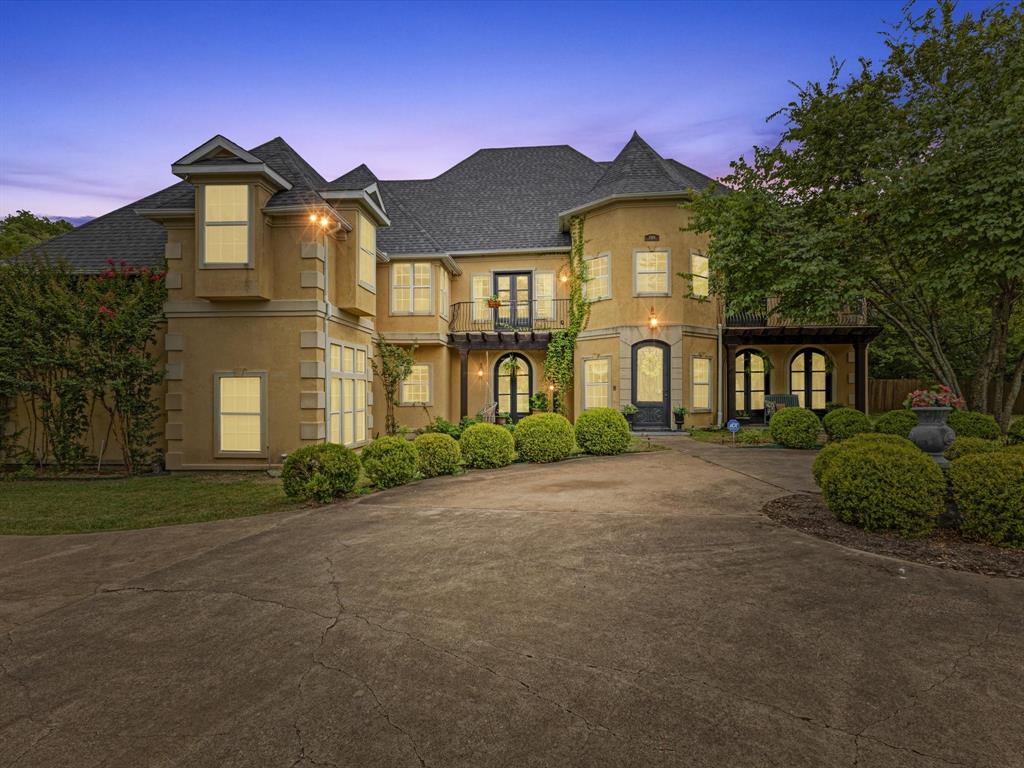 Embrace the romance of Spanish hacienda living in this one-of-a-kind custom estate, nestled on a serene, tree-lined property behind a private gated entry. A circular drive leads to striking Spanish-style double entry doors with arched tops, lited panels, and iron detailing. Turret-inspired architecture, lush landscaping, and charming Juliette balconies create unforgettable curb appeal. Inside, you’ll find soaring ceilings, a grand staircase with iron railings, rich wood floors, and natural light throughout. The main living room features one of two elegant fireplaces and dramatic floor-to-ceiling windows overlooking the scenic backyard. A secondary living area offers a more intimate space with French doors and warm accents, while the formal sitting room is framed by oversized Spanish-style double doors for added grandeur. The open-concept kitchen blends rustic charm with modern function and flows into a formal dining room adorned with chandeliers and arched French doors. Upstairs, the spacious primary suite is a true retreat, featuring a private sitting area, double doors, Juliette balcony, and a luxurious spa-style bath complete with dual vanities, marble flooring, and a freestanding clawfoot bathtub. This home also offers a media room, oversized guest bedrooms, and a large upstairs flex space—perfect as an office, gym, or lounge—with direct access to the breathtaking 872 sq ft open-air balcony for relaxing or entertaining. Outdoor living is equally exceptional with multiple covered patios, a full wraparound porch, and a fully equipped outdoor kitchen. The detached art studio or she-shed features exposed wood beams, abundant windows, and endless creative possibilities. With two fireplaces, a 3-car garage, iron double doors, and thoughtful architectural details throughout, this estate perfectly balances old-world charm and modern luxury.