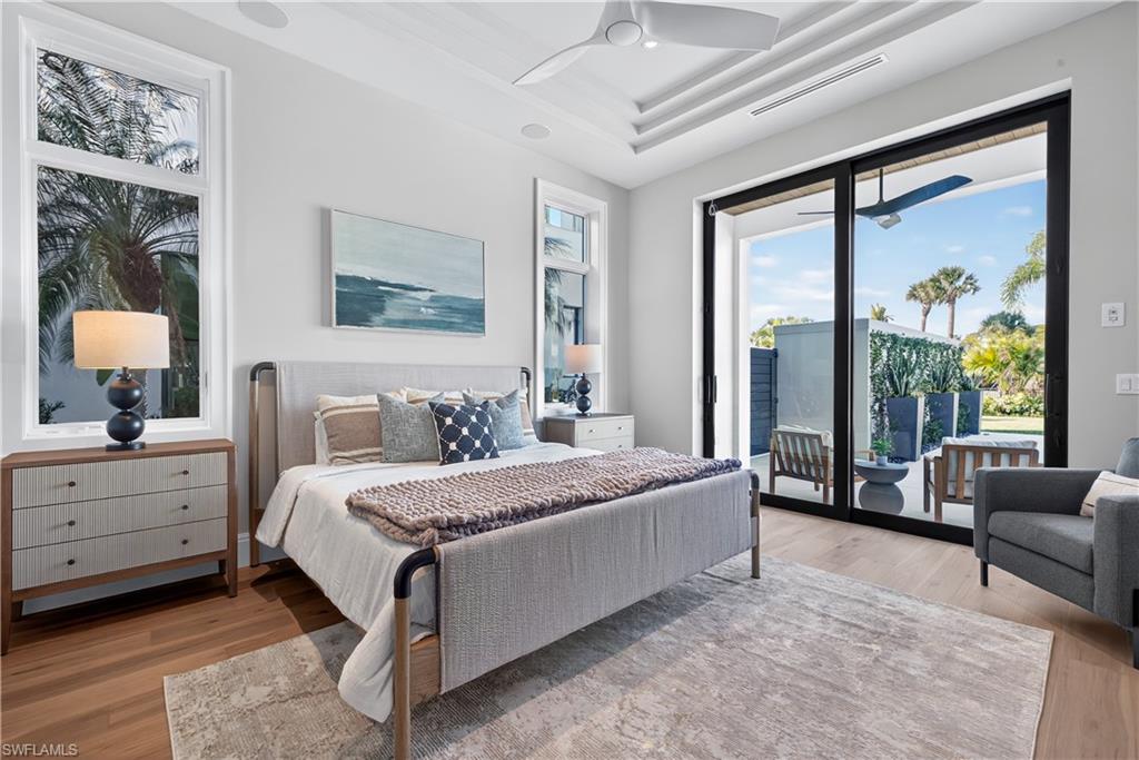 Bedroom featuring access to exterior, light wood-type flooring, a ceiling fan, and a tray ceiling