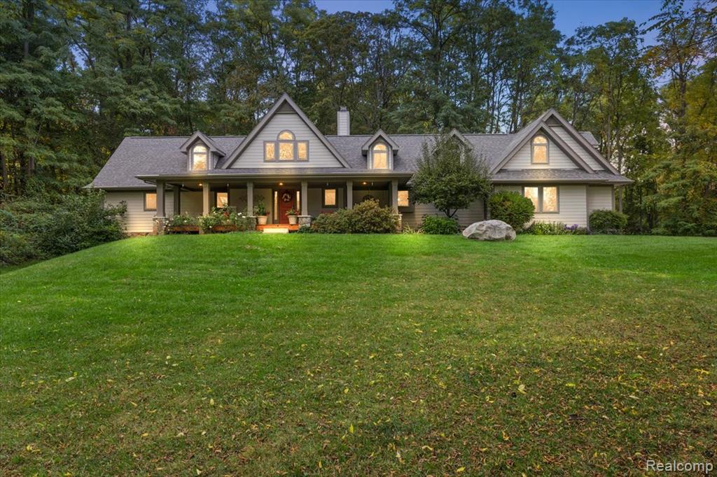Tucked within nine wooded acres in Oakland Township, this bespoke Cape Cod residence offers an extraordinary sense of privacy just moments from the charm of downtown Rochester. Completed in 2013, the home blends classic architectural form with modern function — from its vaulted great room anchored by a stone double-sided fireplace to the seamless flow between kitchen, dining, and gathering spaces.
The main-level suite is retreat living, featuring a spa-inspired bath with jetted soaking tub, glass-enclosed walk-in shower, dual vanities, and a custom dressing closet. Upstairs, two guest suites, a full bath, and a vaulted bonus room with warm wood ceilings create room for reflection, creativity, theater room, or workout room.
A partially finished lower level, plumbed for full bathroom, invites further expansion. While panoramic woodland views from nearly every window establish a continuous connection to nature. The expansive front porch is spectacular and offers a swing to curl up and enjoy your favorite book, watch the wildlife roam, and family play.  Quietly luxurious, undeniably private — this is elevated living with proximity to every convenience.
