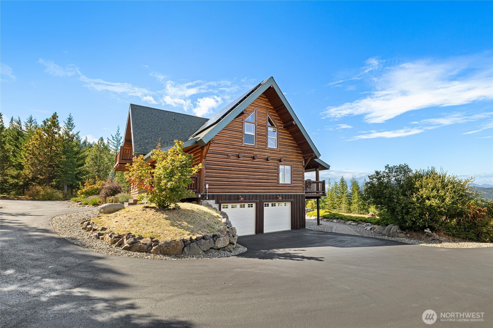 Exterior view showcasing the home’s log architecture, paved drive, and attached two-car garage.