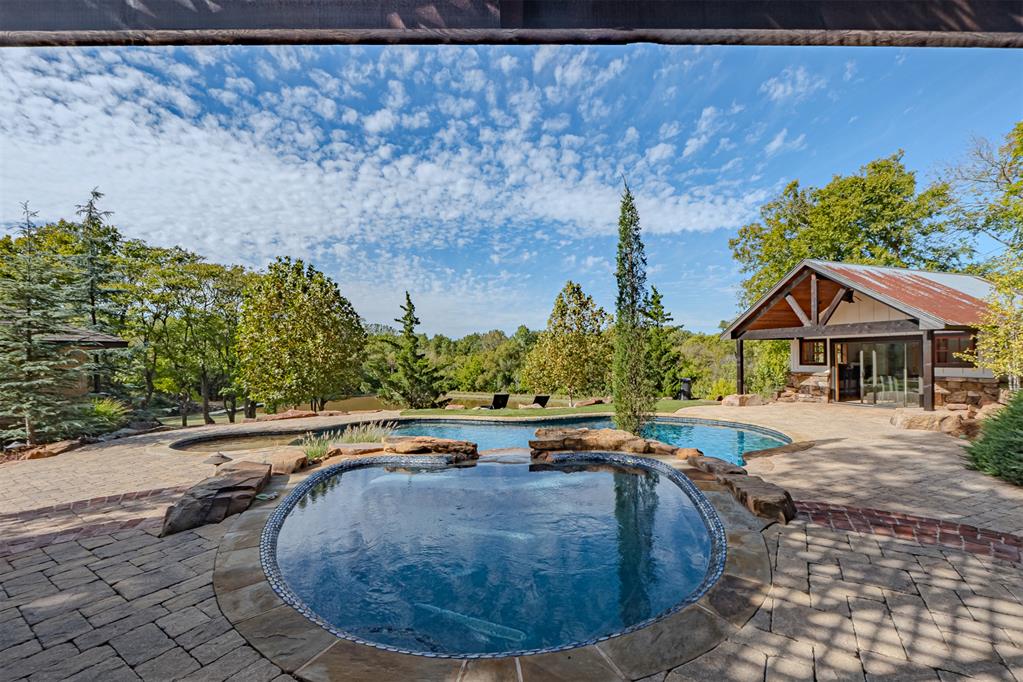 OFFER DEADLINE SAT OCT 24th at 5PM Rich history, an outdoor oasis and sprawling acreage come together in this extraordinary River Oaks property. Brick walkways, inviting covered porches and meticulously cultivated landscaping set the scene before you ever step inside. The sunken living room is crowned with impressive beams crafted from trees harvested on the property, one of many details connecting the home to its remarkable past. The main level offers a spacious primary suite with jetted tub, separate shower and walk-in closet, a kitchen featuring a corner farmhouse sink and casual dining area, formal dining room with custom lighting, powder room, study or optional bedroom, an interior utility room, and a room preserved from the original Land Run homestead. Upstairs, two additional bedrooms, a full bathroom and abundant storage complete the interior. Outside, nearly five acres unfold into a beautifully landscaped retreat with a pond, pool, spa, outdoor kitchen and multiple spaces designed for gathering or simply enjoying the surroundings. A shaded patio overlooks the water, while the pool house provides shaded space and a bathroom with shower. Backing to Corps of Engineers land with no residential neighbors directly behind, the property enjoys exceptional privacy. Geothermal heating and cooling add modern efficiency to a home where original craftsmanship, thoughtful design and an extraordinary setting meet..93 acres comes from a 2nd parcel. Property has been wired for a generator. Pool equipment replaced this year.
