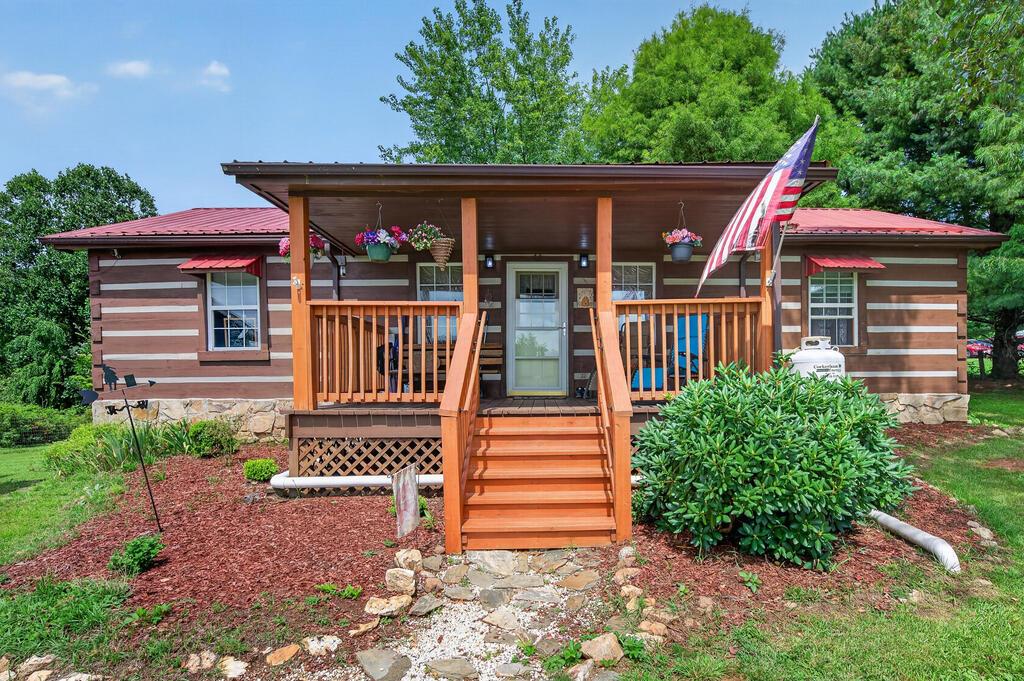 Welcome to a charming log cabin retreat where warmth, comfort, and effortless one-level living come together in a beautifully designed setting. Featuring a desirable split-bedroom floor plan, the heart of this home is the inviting kitchen and living area, highlighted by soaring vaulted ceilings, exposed beams, and a cozy gas fireplace that creates the perfect gathering space. The kitchen combines rustic character with modern convenience, offering beautiful wood cabinetry and newer stainless-steel appliances. Just off the kitchen, an all-season bonus room adds versatile space for a home office, reading room, hobby area, or simply a peaceful place to enjoy the surrounding views. A sliding barn door adds a touch of rustic charm and character. Two spacious bedrooms are privately positioned on opposite sides of the home, each featuring its own en-suite bathroom—ideal for guests, family, or comfortable everyday living. With everything conveniently located on one level, this property is thoughtfully suited for easy living and aging in place. Step outside and discover a property designed for enjoying the outdoors. The completely fenced yard provides privacy and room to roam, while the large garden area offers plenty of space to grow your own vegetables, flowers, or herbs. A grape arbor pavilion creates a delightful spot for relaxing or entertaining, and an additional building with power provides flexible space for storage, hobbies, a workshop, or your next project. Enjoy beautiful sunrise and sunset views while embracing the peace and privacy of your own little retreat. Ideally located just off the Blue Ridge Parkway, you'll have easy access to the charm of Fancy Gap, Hillsville, and Mount Airy. A true blend of rustic character, modern comfort, privacy, and convenience—this is mountain living made easy.