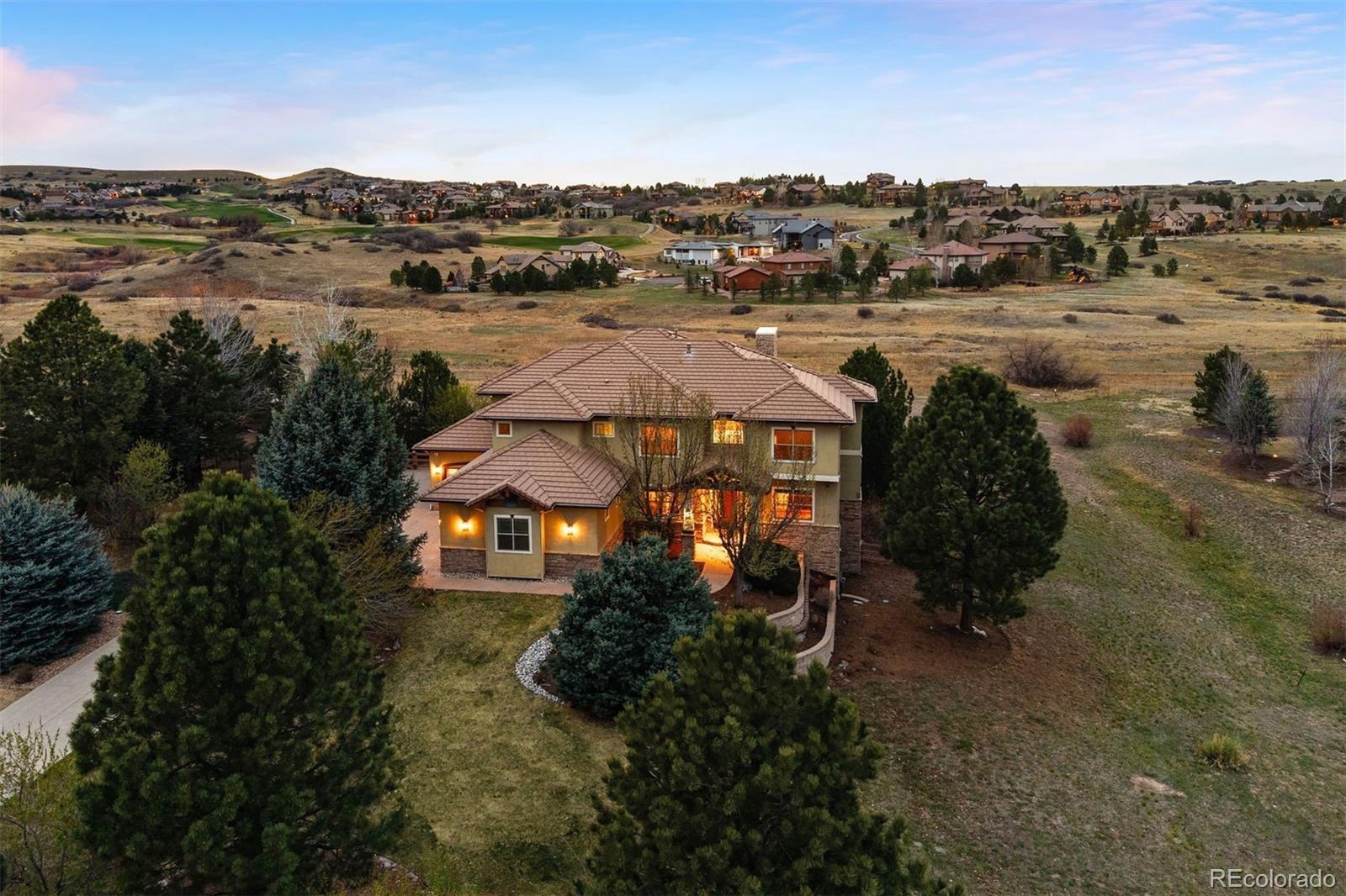 Set on a 1.3-acre lot backing to open space, this Pradera home offers an ideal blend of space, setting, and livability, all with convenient access to Castle Rock and Parker. Inside, an open foyer leads to a two-story great room, anchored by a floor-to-ceiling stone fireplace, with open space views and walkout access to the expansive deck. The kitchen offers ample workspace and storage, featuring updated cabinets with roll-out shelves, dual ovens, dual dishwashers, and a large walk-in pantry. Adjacent is the light-filled breakfast nook which opens to the covered deck, perfect for enjoying your morning coffee or a sunset cocktail. A butler’s pantry with double beverage refrigerators connects seamlessly to the formal dining room with lighted tray ceiling and wood floor inlay. Also on the main level are an office with beam-accented ceiling, a mudroom featuring a built-in bench and cubbies, spacious laundry room, powder bath, and an oversized 4-car garage with excellent capacity for vehicles, toys, and tools. Upstairs, the primary suite offers open space views, with room for a king bed plus seating area. A three-sided fireplace draws you into the en suite bath with soaking tub, separate vanities, dual-head shower, two water closets, and two walk-in closets. Completing the upper level are two additional bedrooms with shared Jack-and-Jill bathroom and one bedroom with en suite 3/4 bathroom, all generously sized and all with walk-in closets. The walk-out lower level is tailored for entertaining, with large rec room, full wet bar, climate-controlled wine room, theater, and a versatile bonus room. Perfect for hosting, there is an additional guest suite and updated 3/4 bathroom. A large, partially covered patio and built-in fireplace extend the Colorado living experience outdoors. With access to the Pradera clubhouse and pool, this is your opportunity to own a home that combines scale, functionality, and lifestyle in one of the area’s most sought-after communities.