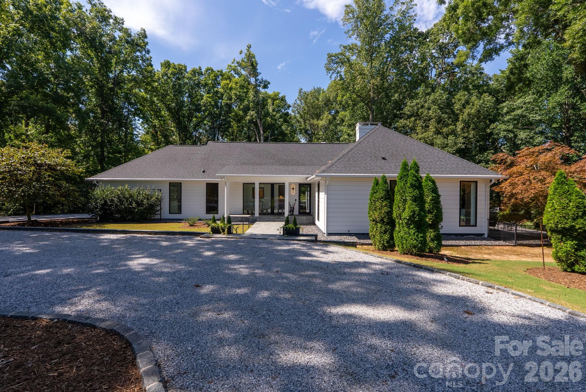 Masterfully reconstructed and redesigned-this extraordinary residence sits on just under two acres in desirable Tryon, NC. Thoughtfully re-built from top to bottom, it is meticulously redesigned for today's lifestyle. Distinctive spaces and refined living feel effortless day to day or while entertaining guests. Expansive windows frame the surrounding landscape and fill the interiors with natural light, bringing the outdoors in while the circular drive and front porch present a warm welcome. The spacious foyer opens to a striking main living and dining area defined by exposed beams, soaring character and an impressive gas fireplace. The open kitchen boasts a Caesarstone island, sleek cabinetry, custom hood, top grade appliances and integrated details. Just off the kitchen, the sophisticated yet hardworking scullery is brilliantly designed for remarkable functionality with custom storage systems, dedicated laundry with sink, and mudroom bench. Another great feature is the built-in dog bath, complemented by a convenient doggie door, open to a separately contained space specifically for beloved pets. The nice climate invites you outdoors where you'll enjoy the spacious deck in this private, natural setting. Plenty of room to enjoy peaceful mornings and relaxing evenings with modern railing overlooking the lush landscape, as well as the side patio and park-like setting. The main floor primary suite accommodates a sitting area, lovely views, walk-in tile shower, heated floors and customized walk-in closet. The fully-equipped study offers beautiful views as well with a second gas fireplace, abundant built-ins and a walk-out to the side patio. A distinctive powder room completes the main floor. The upper level offers a guest bedroom and full bath, walk-in attic, and flex room, ideal for storage or a future bedroom. More highlights include a Generac whole-house generator, technology & security systems, speaker system throughout, and a 2-car side entry garage. All aspects of the home were rebuilt in 2020 including: HVAC, architectural roof, plumbing, electrical, flooring, walls, landscape design, windows, doors, appliances and exterior lighting. Located just moments from local favorites like The Hare & The Hound Pub, Tryon Int'l. Equestrian Center, local wineries, Tryon Theatre, and quaint antique shops. Easy proximity to I-26, I-85 & Hwy 74, Greenville/Spartanburg, Charlotte, Asheville and the Blue Ridge Mountains. Effortlessly move-in ready, this home delivers quality construction and artful character within this inviting community.