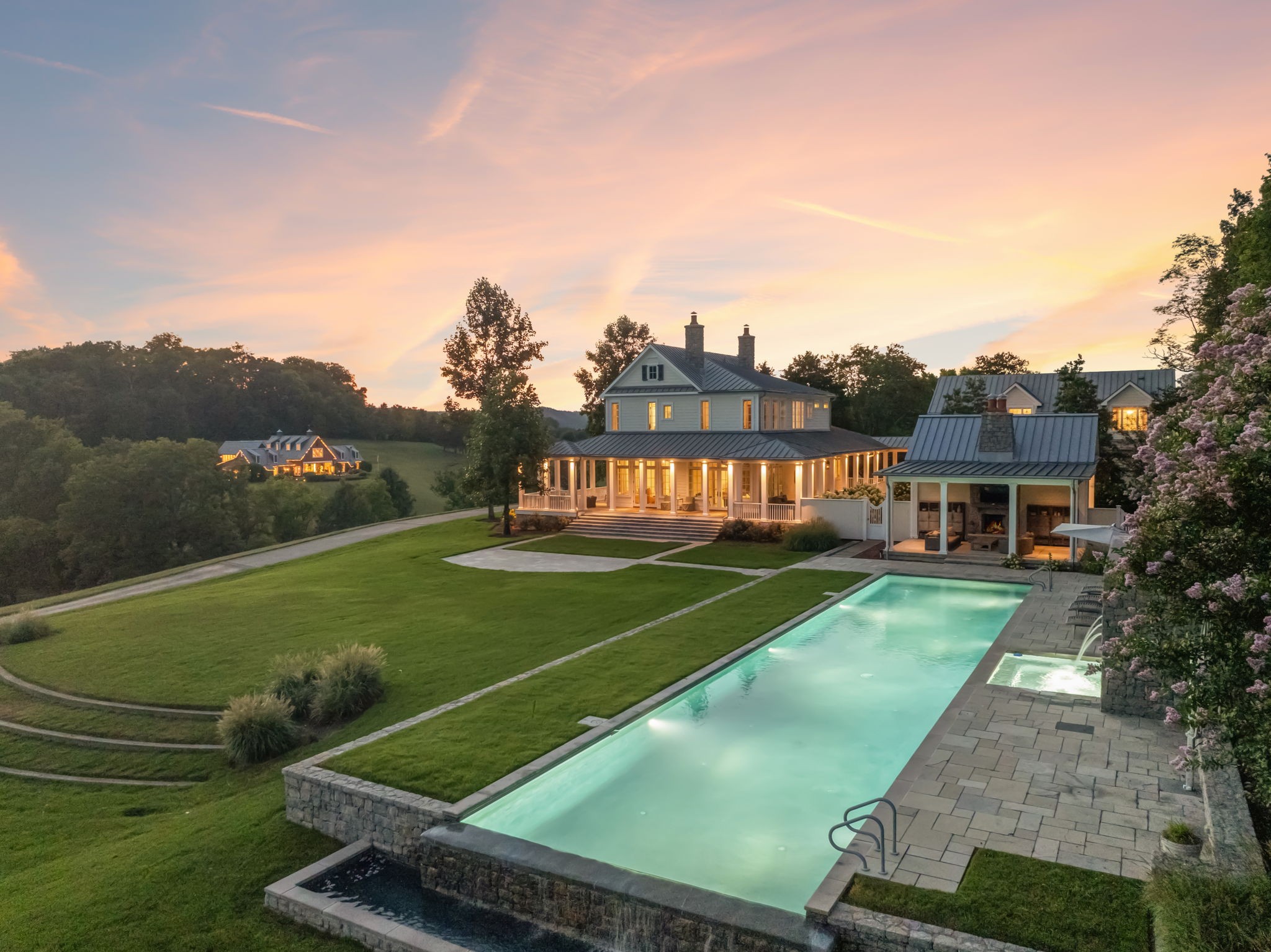 Surrounded by protected Tennessee Land Trust properties and just minutes from Leipers Fork Village, this luxury estate farm offers a rare blend of natural beauty and exquisite craftsmanship designed for effortless indoor and outdoor living. Nearly 40 acres showcase sweeping views of rolling hills, two stocked ponds, grazing pastures, an organic vegetable garden, walking trails, and endless privacy. Designed for both relaxation and entertaining, the estate features a saltwater infinity-edge pool, a Gavin Duke–designed poolside cabana with stone fireplace, and a stunning formal garden with fountain adjacent to the outdoor kitchen and dining area.

The main residence, 3385 Bailey Road, is as timeless as it is elegant. With its large wraparound porch, you’ll capture both sunrise and sunset. Inside, the home features a great room ideal for entertaining, three upstairs ensuite bedrooms, a main-level office/guest room, and a chef’s kitchen that serves as the heart of the home. Three fireplaces add warmth and character throughout. A full guest apartment with a private entrance, living room, kitchen, and bedroom sits above the oversized 3-car garage.

Across the property is the “77” Entertainment Barn, which is nothing short of extraordinary. Designed by architect Eric Stengel, this 5,300 sq. ft. masterpiece combines rustic character with refined luxury. Soaring ceilings frame an open space anchored by a grand imported bar with large video wall, and two stone fireplaces—perfect for both large and intimate gatherings. Two private bedroom suites, each with a fireplace, laundry, and kitchenette, flank the great room, while a game room, full upstairs catering kitchen, gym, bathroom, and oversized 2-car garage provide modern convenience. Adding to its prestige, a Gary Hedden–designed recording studio makes this barn a destination for creativity and entertainment. The “77” is truly one of Leipers Fork’s most remarkable spaces.
Option to purchase fully furnished.