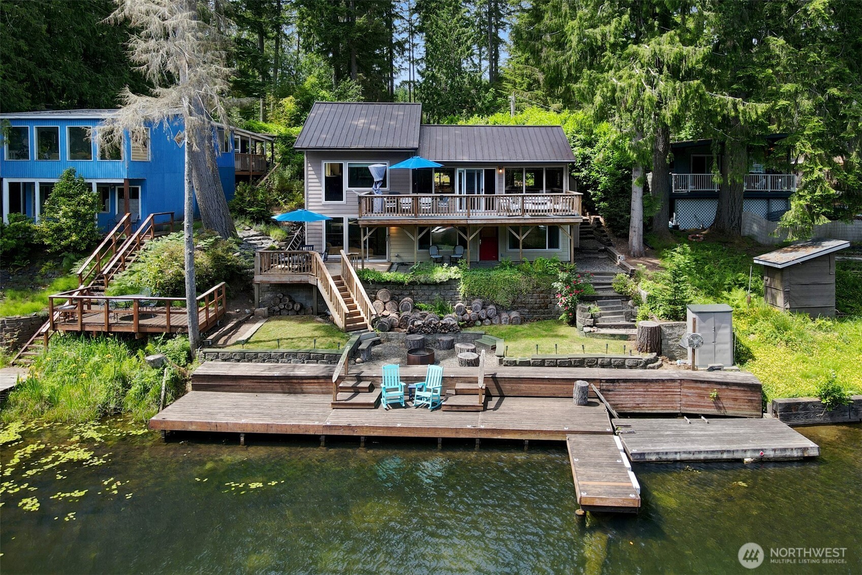 This Haven Lake home offers 62 feet of lakefront, a private dock, and views from nearly every room. The main floor has an open layout with an eat-in kitchen, large dining area, and living room that opens to a full-width deck overlooking the water. The main-level primary includes an ensuite private bath with walk-in shower. Downstairs, the daylight basement adds flexibility with a second bedroom, a flexible office or den space (could be a 3rd bedroom!), and a large bonus room with attached extra large storage. Doors lead to the lower decks complete with a fire pit and easy lake access. Short drive to Belfair for all amenities.