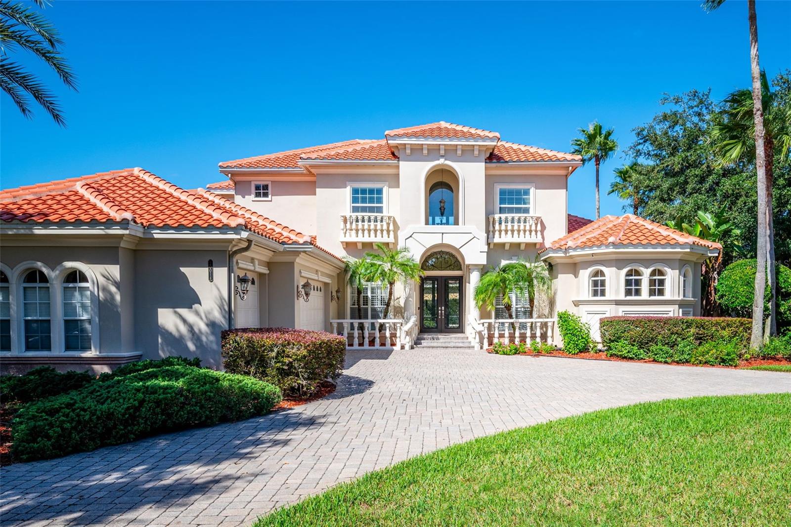 Virtually Staged. Mediterranean elegance meets resort-style living in this exceptional estate, privately positioned on a tranquil pond in the sought-after gated community of Grand Hampton. From the grand circular paver driveway and stately balustraded entry to the wrought-iron double doors, the home makes a memorable first impression. Inside, a breathtaking two-story living room welcomes you with soaring ceilings, expansive windows overlooking the pool, a marble-surround fireplace, and a sweeping wrought-iron staircase. Coffered ceilings, crown molding, large-format tile, and plantation shutters add timeless character throughout the main living areas.Perfect for both intimate gatherings and grand entertaining, the formal dining room showcases a coffered ceiling, crystal chandelier, elegant wainscoting, and an arched window. At the heart of the home, the gourmet kitchen features a generous center island, stainless steel appliances, and abundant updated cabinetry, with an easy transition to the sunlit breakfast nook and oversized family room. The open layout creates a natural gathering space where everyday living and entertaining come together effortlessly.The main-level primary suite offers a peaceful escape, featuring a bayed sitting area, tray ceiling, and an impressive spa-inspired bath. A mosaic-tile arch frames the central soaking tub, complemented by dual vanities, large walk-in shower, and spacious walk-in closets. A private guest bedroom with guest bath, a light-filled office with an arched window, dedicated pool bath, and laundry room complete the first floor.Upstairs, enjoy movie nights in the spacious media room with theater seating, while two additional bedrooms provide flexibility for family and guests. The open overlook to the living room below adds architectural interest and enhances the home's bright, airy ambiance.Step outside to discover your own private retreat. The screened lanai features a sparkling pool and raised spa with fountain, surrounded by lush, mature landscaping and tall hedges for added privacy. A custom stone outdoor kitchen with a built-in grill, vent hood, and refrigerator makes al fresco dining and entertaining a pleasure. Towering oaks, mature palms, and peaceful pond views complete this serene outdoor setting.Thoughtful extras include owned solar panels on the new (2026) barrel-tile roof to help manage energy costs and a three-car garage with ample space for vehicles and storage.Life in Grand Hampton extends well beyond your front door. Residents enjoy a 24-hour guard-gated entrance and an impressive collection of resort-style amenities, including a heated pool with waterslide, fitness center, clubhouse, lighted tennis courts, pickleball and basketball courts, scenic walking trails, and community events coordinated by an on-site Lifestyle Director.Conveniently located near I-75, AdventHealth, Wiregrass Ranch, Tampa Premium Outlets, top-rated schools, colleges, golf courses, athletic clubs, restaurants, and hospitals, this remarkable home offers an exceptional blend of privacy, architectural beauty, and a lifestyle designed to be enjoyed.
