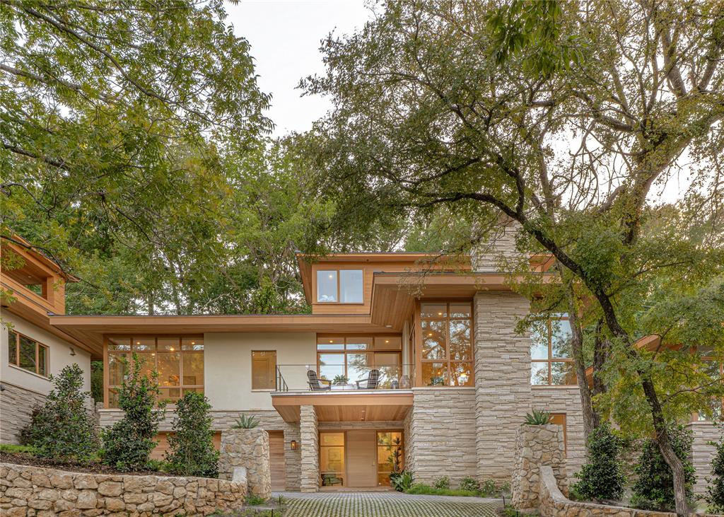 An architecturally striking residence by Blue Quail Builders with architecture by V Fine Homes, this Quail Run home pairs thoughtful modern design with a setting shaped by its natural surroundings. Drawing inspiration from Frank Lloyd Wright’s Fallingwater, the residence was designed to work with the hillside rather than against it, incorporating organic stone, red grandis wood siding and smooth LaHabra stucco for a warm, modern exterior. Inside, expansive floor-to-ceiling windows bring the outdoors into nearly every level, filling the home with natural light and framing views of the surrounding trees. Three distinct outdoor living spaces extend the architecture into the landscape, including a third-floor terrace set among the tree canopy that creates a unique setting for entertaining or unwinding. Spanning 3,205 square feet, the floor plan balances clean architectural lines with open, functional living spaces. A private elevator connects all levels, adding convenience while maintaining the home’s streamlined design. Privacy was also carefully considered throughout, creating a residence that feels tucked away while offering the ease of a lock-and-leave lifestyle. Distinctive architecture, natural materials and a strong connection to its setting define this Quail Run home, all just moments from some of Fort Worth’s best shopping, dining and amenities.