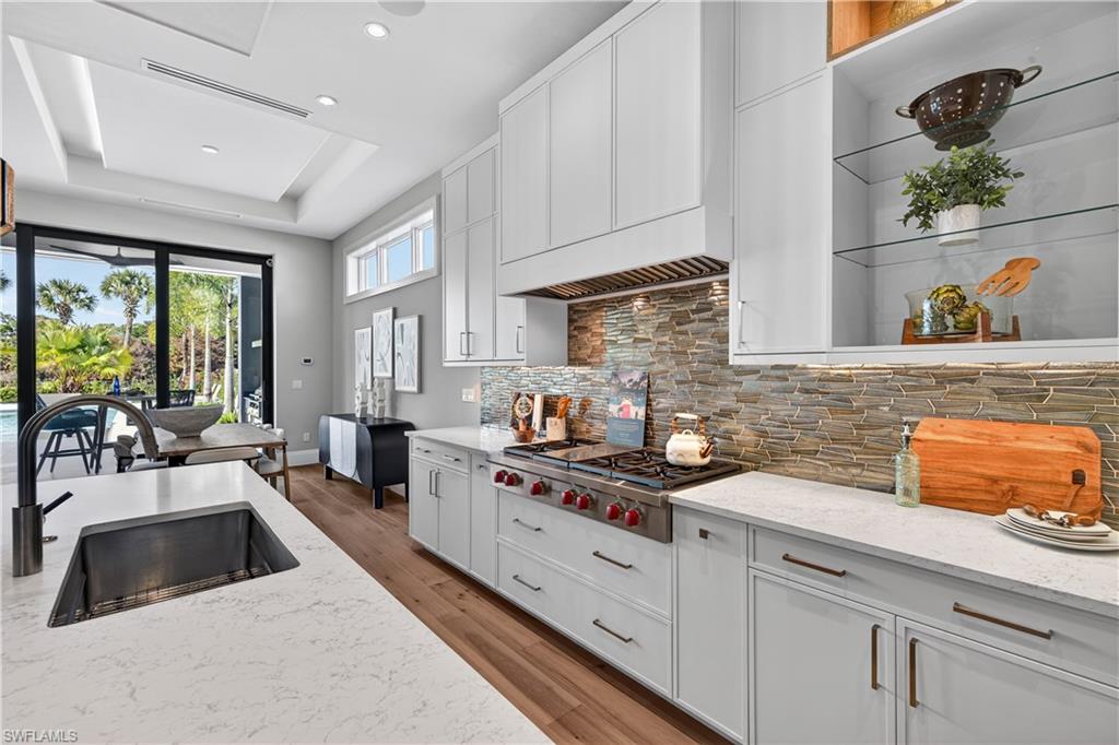 Kitchen with white cabinets, light stone counters, light wood-style flooring, stainless steel gas stovetop, and a raised ceiling