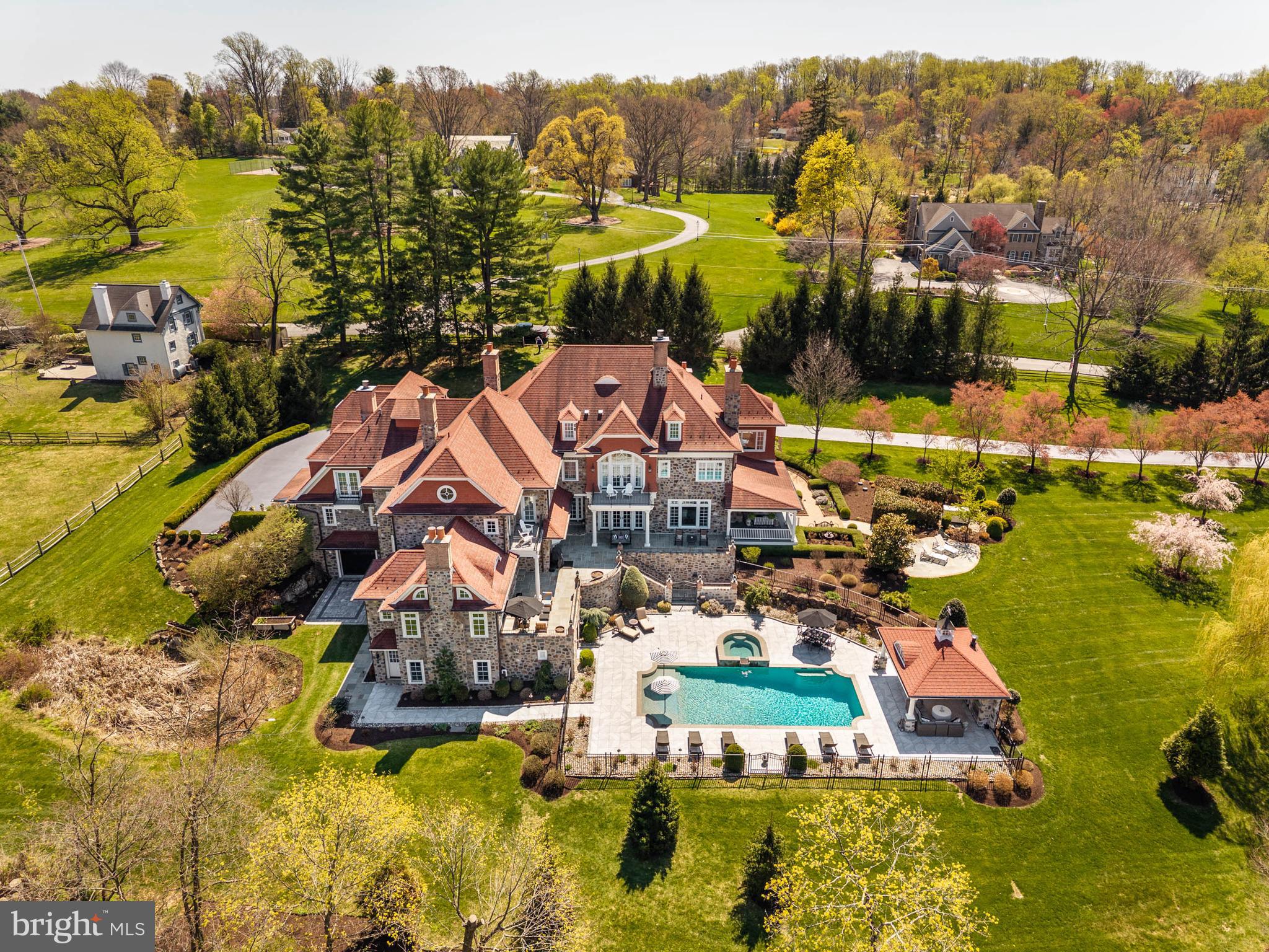 Set on approximately 12 acres, this exceptional stone home follows the tradition of the Main Line’s great country estates—designed for space, scale, and a lasting connection to the land. Built by highly regarded Ted Babiy of Diamond Construction, the residence reflects a level of craftsmanship and materials not typically found in newer construction, with architecture rooted in the proportions and detail of earlier homes.A long, winding approach leads through stone entrance piers to a front courtyard, creating a gradual sense of arrival.The entry opens to interiors marked by quality, warmth, and thoughtful design. The living room features a beamed ceiling, fireplace, and windows and glass doors on multiple exposures, filling the space with light and opening to the surrounding terraces. The dining room is grand in scale, with a coffered ceiling and two sets of French doors that open to a side courtyard with a fireplace, extending the dining space outdoors for entertaining.At the center of the home, the kitchen, breakfast room, and family room connect seamlessly, designed for both everyday living and gathering. The kitchen is expansive, with a large marble-topped center island, custom cabinetry, high-end appliances, and a fireplace that anchors the space. The family room includes a fireplace and beamed ceiling, along with a distinctive inglenook seating area, creating a sense of comfort within its volume while opening directly to the terrace.A sunroom provides a bright, inviting space framed by arched windows and French doors that open to the terrace, creating a direct connection to the outdoors. The first-floor home office features a vaulted ceiling, custom millwork, and a fireplace, combining functionality with architectural presence.Multiple staircases and an elevator connect the main level to both the second floor and the lower level, supporting the home’s scale and allowing for efficient movement throughout.The second floor includes seven bedrooms, including the primary suite and additional bedroom suites, with one currently used as an exercise room. The primary suite functions as a private retreat, with a vaulted-ceiling bedroom and fireplace opening to a balcony overlooking the grounds. A separate sitting room is wrapped in windows on multiple exposures, capturing sweeping views and light throughout the day. Dual baths and generous dressing areas complete the suite.The lower level is designed as a full extension of the home’s living space, featuring a large recreation room, wet bar, home theater with custom seating, wine cellar, and a bath.The outdoor setting captures the property’s long views. A rear flagstone wrap-around terrace—partially covered to create true outdoor rooms—extends from multiple interior spaces, including a covered terrace off the sunroom with a fireplace. Additional terraces, including one accessed from the family room, are positioned to capture those views.Natural features—including a stream, arched bridge, and restored mill structure—add character and depth rarely found in combination on the Main Line.The landscape is defined by sweeping lawn, mature plantings, and carefully composed gardens. A pool and separate cabana with outdoor kitchen and fireplace create a complete setting for outdoor living, all integrated seamlessly into the property’s surroundings.A portion of the property is subject to a conservation easement with the Willistown Conservation Trust, preserving open meadows, mature trees, and natural habitat while limiting future subdivision. Details available upon request.Properties of this scale, setting, and level of construction are increasingly rare—offering a combination of land, design, and craftsmanship that is not easily replicated.