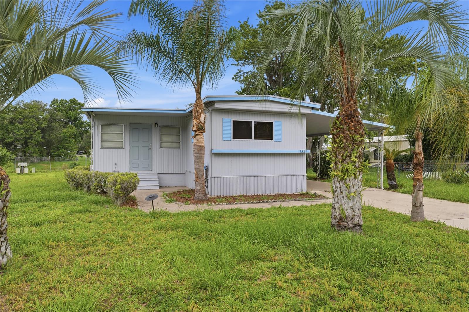 Virtually Staged. FRESHLY PAINTED INTERIOR! Additional comfort and value are provided by two separate air conditioning systems, including a dedicated mini-split unit in the primary bedroom and a central air conditioning system serving the remainder of the home. Framed by mature palms and open green space, this inviting manufactured home offers comfort, versatility, and classic Florida charm on a generous 0.18-acre lot. An elevated entrance, concrete walkway, expansive front yard, and large front-facing windows create an inviting first impression, while the screened front porch provides a comfortable place to enjoy the outdoors year-round. The newly renovated kitchen features all-white cabinetry, matching white appliances, granite-look countertops, a double-basin sink, and built-in storage, creating a bright and functional space for daily living. Inside, engineered hardwood flooring flows throughout much of the home, creating a cohesive and easy-to-maintain living environment. The oversized primary bedroom offers exceptional flexibility with multiple windows that bring in abundant natural light, built-in storage, a dedicated mini-split air conditioning unit, and ample space for a sitting area, home office, or hobby space. Another generously sized bedroom features wood-look wall paneling, a large window, window blinds, and convenient access to a nearby bathroom. The third bedroom provides additional versatility with laminate flooring, multiple windows, a ceiling fan, built-in cabinetry, drawers, and a spacious closet, making it ideal for guests, remote work, or creative pursuits. The home's bathrooms are thoughtfully designed for everyday comfort and functionality. One bathroom features an enclosed shower with a textured glass door, vanity storage, an attractive countertop, and a single-basin sink, while the second bathroom offers a tub and shower combination, a single vanity with storage, concealed medicine cabinet storage, durable countertops, bright vanity lighting, and a natural light window positioned above the tub. Adding even more practicality, the dedicated laundry and utility room includes washer and dryer connections, a utility sink, wall shelving, pegboard organization, concrete flooring, and abundant space for storage, hobbies, crafts, or workshop activities. Outside, the generous backyard is surrounded by mature shade trees and open green space, providing endless possibilities for gardening, pets, entertaining, or future improvements. A concrete patio area offers the perfect place for outdoor seating or grilling, completing a property that blends comfort, functionality, and the relaxed Florida lifestyle.