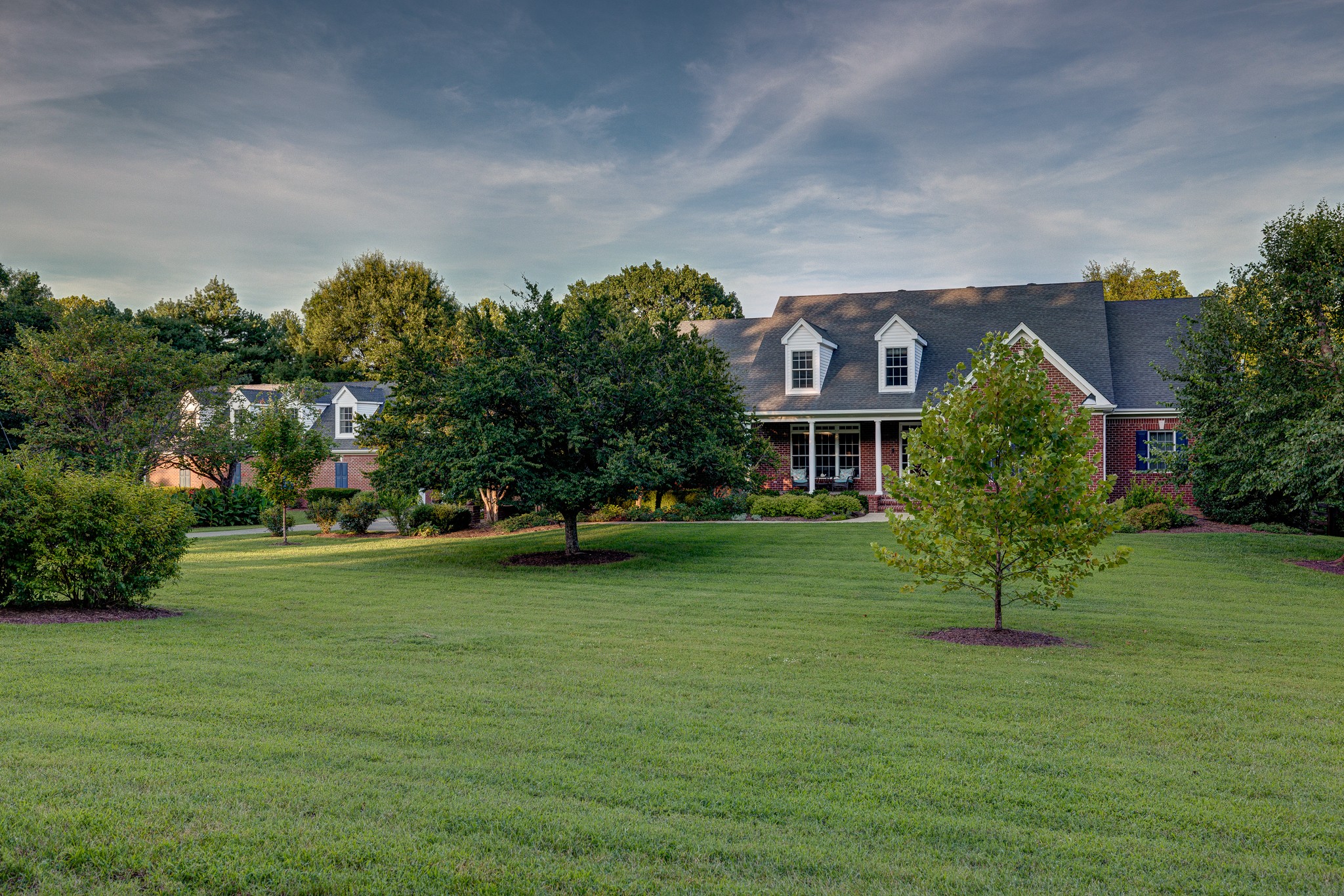 Three properties in one: a luxury residence, a multigenerational retreat, and a workshop/collector compound. On 5.1 private, wooded acres, the all-brick home provides almost 9,000 heated and cooled square feet, including 2 main-level suites and a 3,438-square-foot walk-out basement. A powered outbuilding/workshop adds approximately 3,300 square feet under roof for cars, equipment, hobbies and storage.Inside, a vaulted great room centers on a floor-to-ceiling stone fireplace. Separate living and dining rooms add coffered and tray ceilings, and the kitchen includes granite counters, a 6-burner cooktop, double ovens, warming drawer, pot filler and 48-inch built-in refrigerator. The primary suite has a walk-in closet and bath with steam shower, garden tub and double vanities. Upstairs are 2 additional bedrooms with private baths, a rec room and media room with refreshment area.The walk-out basement drives the home's multigenerational flexibility. Seven windows and French doors bring in natural light across 2 living areas, a kitchenette without a range, office, full and half baths, flex/work areas and storage. Its separate exterior entrance opens to a covered lower patio.The full-brick detached building delivers the collector/workshop side of the property: 3 overhead doors, an air-conditioned workshop, 120/240V power, work sink, cabinetry, half bath, epoxy-coated floors and a fully decked upper level. A tall-clearance carport adds room for oversized vehicles or recreational equipment.Established trees, landscaping, gardens and covered outdoor spaces complete the setting. With no HOA and access to I-24, the south Davidson County location offers a broader Greater Nashville option—especially for those comparing acreage properties across Nashville, Brentwood, Nolensville, Franklin and Murfreesboro or relocating to Middle Tennessee. One address combines privacy, flexible living and serious workshop capacity.