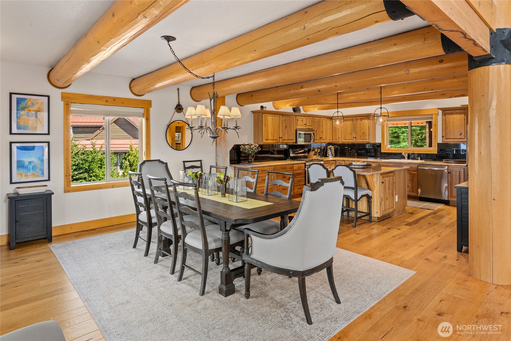 Spacious kitchen with granite countertops, warm wood cabinetry, stainless appliances, and a large center island beneath exposed log beams.