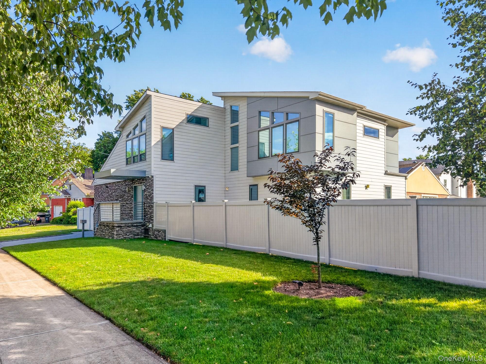 Welcome to a rare fusion of residential elegance and a contemporary masterpiece. Built in 2014, this 3,343 sq. ft. home is defined by its meticulous attention to detail, open-concept flow, and unexpected design touches that set it far beyond traditional new construction. Set on a sprawling 7,029 sq. ft. lot, this property offers ample outdoor space while maintaining a low-maintenance, sophisticated lifestyle.From the moment you step inside, hardwood floors run continuously throughout the main and upper levels—no carpet, no transitions—creating a seamless, warm, and visually expansive foundation. The open kitchen is both a work of art and a serious cooking space. Sleek, slab-style modern cabinetry stretches to the ceiling, offering abundant storage, while the full suite of Viking appliances—including a professional-grade gas range, stainless steel refrigerator, and vented hood—promises restaurant-quality performance. A large island anchors the space, perfect for casual dining or hosting. Adding to the home’s impressive functionality are two commercial-grade A/C units on the first floor, delivering powerful, zoned cooling and heating that ensure year-round comfort no matter the season.All bedrooms are genuinely oversized, each comfortably accommodating a king-sized bed with room left for nightstands and dressers. Two of these bedrooms feature private ensuites, finished with premium tile, floating vanities, and luxurious in-floor radiant heating. In total, three bathrooms feature heated floors, a coveted amenity that transforms cold mornings into a spa-like experience.Descend to the lower level, where a dedicated movie theatre awaits. Thoughtfully designed with plush seating, attached projector and screen, and dimmable lighting. The basement also offers flexible space for a gym or play area, while above, you’ll find living areas on both the first and second floors, giving you the rare flexibility of a formal parlor or second-floor family lounge.Step outside to enjoy two distinct outdoor escapes: a private balcony off one of the second floor, ideal for morning coffee, and a rear deck for grilling and al fresco dining. The exterior is clad in low-maintenance, ultra-durable James Hardie Fiber Cement siding, chosen for its resistance to moisture, fire, and pests.Perhaps the home’s most distinctive feature is the custom metal railing system—designed, fabricated, and installed by a welding company that typically builds roll cages and chassis components for race cars. These railings are not off-the-shelf. They feature precision welds, automotive-grade finishes, and a sleek, industrial aesthetic that complements the home’s contemporary lines. Every baluster and handrail feels engineered for strength and beauty.For total security and peace of mind, the property is monitored by a discreet network of 8 exterior security cameras, covering every approach, entrance, and blind spot. Whether you’re home or away, you remain in complete control.Location is everything, and this home delivers. You are just minutes from the Long Island Rail Road, making your commute to the city effortless and stress-free. And when it's time to unwind, enjoy proximity to nearby golf courses, perfect for weekend getaways or after-work tee times.This is not a cookie-cutter modern home. It’s a thoughtfully built, one-of-a-kind property where race-car precision meets everyday luxury.