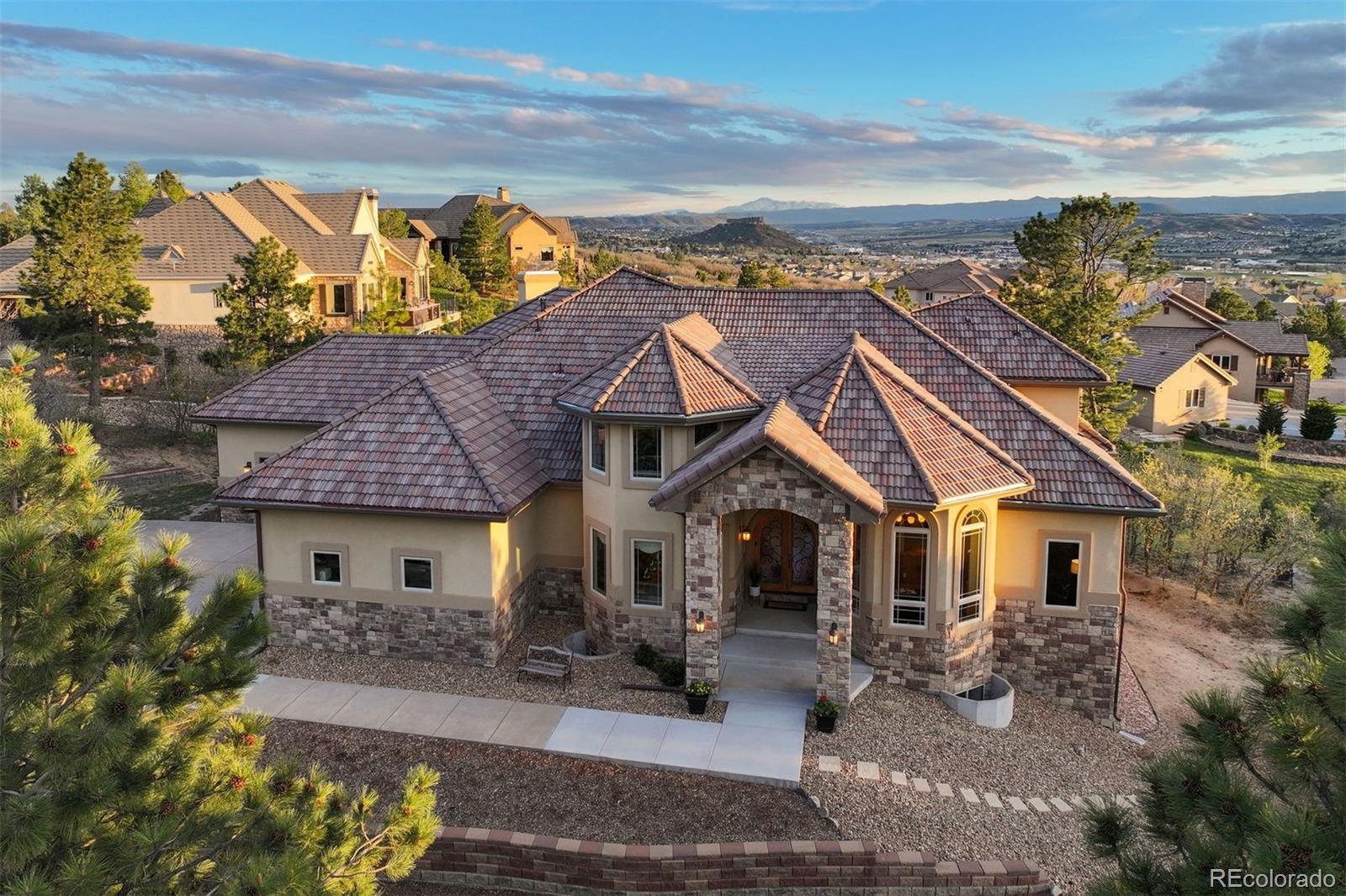 Pikes Peak and Castle Rock's namesake "Rock" share a single view, and here, you have the best seat for it! Privately positioned within Piñon Soleil, the home is designed to take in the view while staying sheltered in its setting, made for easy living both indoors and out. Castle Rock, Parker, and Denver are all close at hand, so dining, shopping, and daily essentials are never far. Curved walls, soaring ceilings, and rich layers of timber, stone, and brick create a sense of warmth and character. Double-arched front doors open to a sunlit foyer and great room, where a two-sided fireplace and walls of glass frame the mountain views. Cherry floors carry you through the main level and into a chef’s kitchen featuring high-end appliances, a generous island, a walk-in pantry, and a brick fireplace that naturally draws people in. Surrounded by windows, the eat-in area feels relaxed for daily living, while the formal dining room offers an elegant setting for hosting.This home offers the flexibility of two spaces that could serve as a primary suite, depending on how you live. The upper level provides a serene retreat with a private balcony, dual walk-in closets, a fireplace, and a spa-like bath. A clawfoot tub rests within a turreted bay window, perfectly positioned to take in the views. On the main level, a guest suite with its own five-piece bath and mountain outlook offers an equally comfortable option for main-floor living or long-term guests.The walk-out lower level is designed for entertaining and everyday enjoyment, with a spacious recreation room, wet bar, theater, and dedicated gym space. Outside, the flat backyard opens up new possibilities, from a future pool or garden to simply enjoying the space as-is. A four-car garage, circular drive, and additional parking add convenience. This is Colorado living at its most refined, elevated, private, and designed for a life well lived.