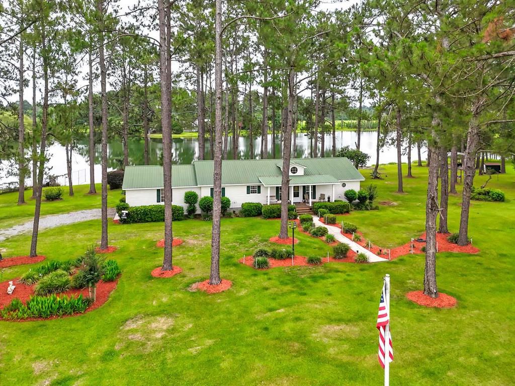 Welcome to your private waterfront retreat! This well-built home sits on a beautiful pond offering stunning water views, peaceful surroundings, and exceptional outdoor living. Enjoy relaxing mornings and breathtaking views from the expansive screened-in back porch overlooking the water, or take in picturesque views of the neighboring horse pasture from the welcoming front porch. Outdoor enthusiasts will appreciate the covered boat and equipment shelter with a concrete floor, dedicated fish cleaning station, and multiple outbuildings providing abundant storage for tools, recreational gear, and lawn equipment. The beautifully manicured property features an irrigation system, strategically placed electrical outlets for seasonal displays, and a serene setting tucked down a quiet gravel lane for ultimate privacy. Inside, the spacious open-concept floor plan showcases high ceilings, abundant natural light, and comfortable living spaces perfect for entertaining. The well-appointed kitchen offers extensive cabinet storage, a large pantry cabinet, hard-surface countertops, and scenic pond views from the kitchen window. A generously sized laundry room adds convenience, while the second full bathroom is ideal for guests or children. The oversized owner's suite features a spacious bedroom, walk-in closet, and large bathroom complete with dual vanities, a soaking tub, and a tiled walk-in shower. Additional storage can be found above the carport and within the two outbuildings. A durable metal roof provides long-lasting peace of mind, making this exceptional waterfront property the perfect blend of comfort, functionality, recreation, and country living.