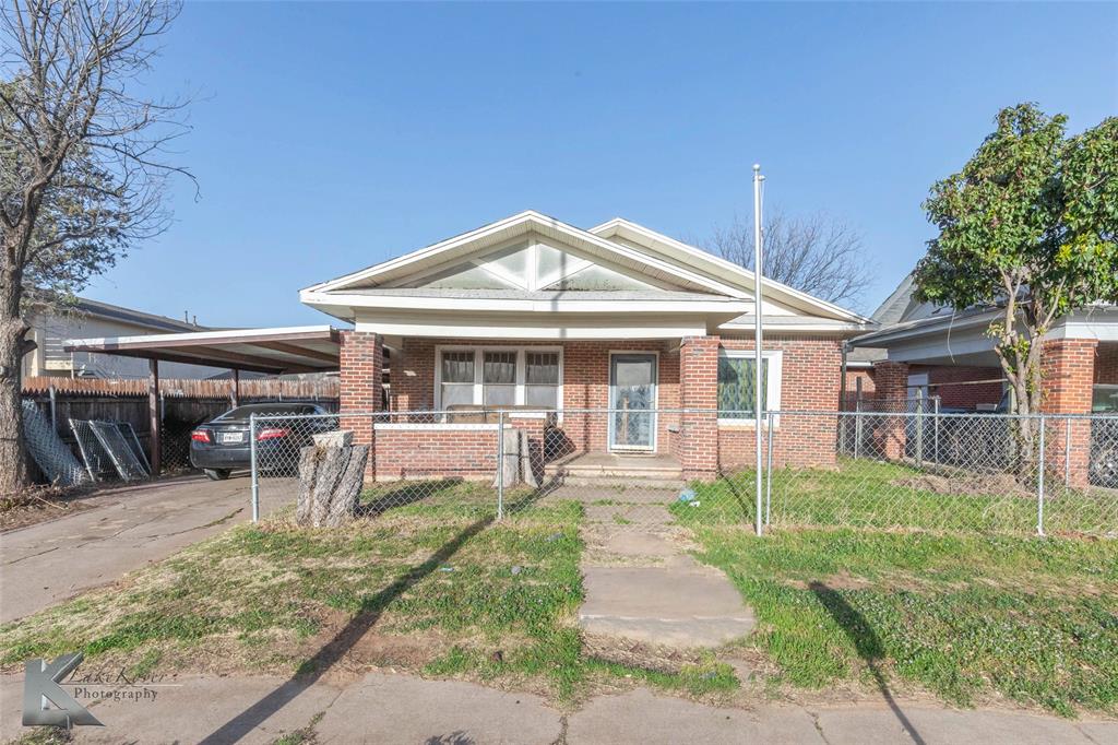 Bungalow featuring driveway, a fenced front yard, covered porch, an attached carport, and brick siding