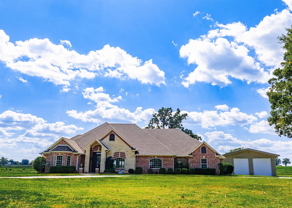 Tucked away, near the Country Club on 20 lush acres you'll discover this magnificent 3 bedroom, 3 full bathrooms and a separate 40x40 insulated workshop! Once inside, you'll find a formal dining room to the right with a trey ceiling and a 12x12 office to the left that can easily be used for a 4th bedroom. Stay toasty on winter nights with a stone-n-brick gas-log fireplace--a center piece in the living on one wall and a wall of windows on the other. An abundance of storage space, granite countertops, electric cooktop, stainless steel appliances, double oven, dishwasher, microwave, breakfast bar, and walk-in pantry with custom shelving, makes this kitchen a dream to cook in. A breakfast area provides additional seating for those large gatherings and also has access to the back patio. With a split bedroom design, the primary ensuite includes a trey ceiling, access to the back patio, separate double sinks, vanity area, separate tub, walk-in shower, and large walk-in closet with custom built-ins. Two guest bedrooms share a Jack-n-Jill bathroom. Additional inside perks are HIGH SPEED FIBER INTERNET, stone accents, laundry room with custom built-ins, recessed lights, closets with automatic lights, 2-car attached garage, double ceiling fans in the living room, ceiling fans in the bedrooms. Carpet has been removed and is ready for the new owners vision for flooring. Outside on the back patio under a vaulted ceiling, you'll find a spectacular outdoor living area with a griddle, pizza oven, refrigerator, sink, bar seating, grill, and unique gas-flame fire feature! Plus plenty of room for outdoor furniture. A detached workshop comes with electricity, water, and 20x30 lean-to area with electric and plumbing. Plus, there is a pond, pasture for livestock, built-in sprinkler system, and concrete driveway. Modern amenities, inside this 2,832 square feet of custom living, is found on scenic acreage in the beautiful countryside of southern Hopkins County!