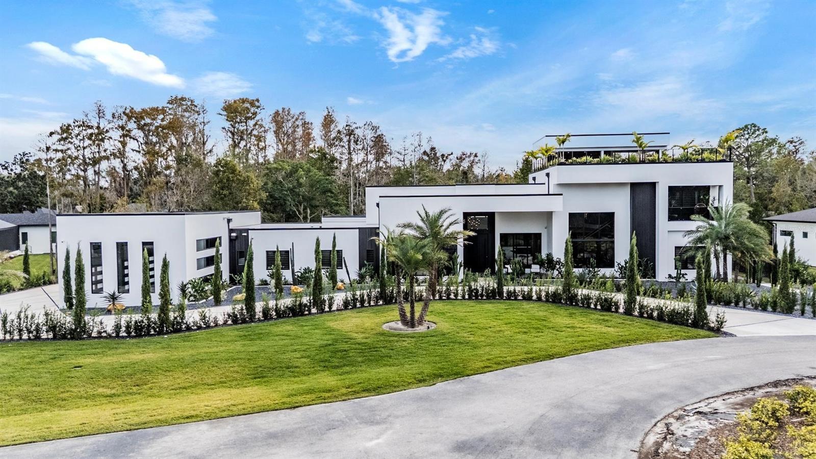Welcome home to this stunning state-of-the-art exceptional estate. Positioned on a private 1.31-acre sanctuary in the gated enclave of Grande Estates, this architectural masterpiece stands as a triumph of modern luxury, offering 6 bedrooms, 7.5 bathrooms, and 7,421 square feet of meticulously tailored living space. From the moment you arrive, the residence makes an unforgettable impression with its striking geometric lines, warm wood-toned soffits, and dramatic floor-to-ceiling glass grids. A sweeping driveway with custom geometric linework guides you past mature date palms and sculpted cypress borders toward a grand, sheltered entrance and a multi-bay showroom garage finished with a pristine high-gloss custom coat.Inside, an oversized matte-charcoal pivot door opens to a double-height foyer where an indoor Zen stone garden sits beneath a floating glass-and-timber staircase and a floor-to-ceiling book-matched marble wall. Mirror-like porcelain floors run continuously into the main living gallery, where glass pocket doors vanish to merge the interior with the patio. The culinary domain centers on dual waterfall-edge quartzite islands, handleless matte-charcoal cabinetry, and a secret pivot door that opens into a hidden butler's pantry. Nearby, the dining space is framed by a custom backlit wine display wall and bathed in warm light from cascading glass pendants.The primary wing serves as an opulent private sanctuary, incorporating a dedicated sitting lounge, rich vertical wood paneling, and a high-gloss boutique wardrobe room with integrated LED illumination. In the en-suite bath, a sculptural dark-slate soaking tub, floating vanities with backlit wavy mirrors, and a dark marble rainfall shower deliver an authentic spa experience. Health and vitality are prioritized with a private dry cedar sauna powered by a Harvia stove and a dedicated home fitness space.Outdoors, a soaring panoramic screen cage encloses an extraordinary resort-style haven. The L-shaped blue mosaic pool features an integrated spa, deck jets, and a sheet waterfall cascading from the upper overhang. Entertaining is effortless with a full outdoor kitchen wrapped in dark quartz, a linear electric fireplace media wall, and a wet bar. Above it all, an exterior staircase leads to a rooftop sky terrace with composite decking, glass railings, and a covered bar framing views of the lush forest canopy. Beyond the gates of this exclusive community, Grande Estates offers unparalleled privacy and serene natural surroundings while providing seamless connectivity via I-275 and US-41. This prime Lutz location places top-rated schools, premier shopping and renowned golf courses such as Avila and Carrollwood Country Club and Downtown Tampa all within quick reach. Schedule your private tour today to experience this amazing luxury lifestyle firsthand!