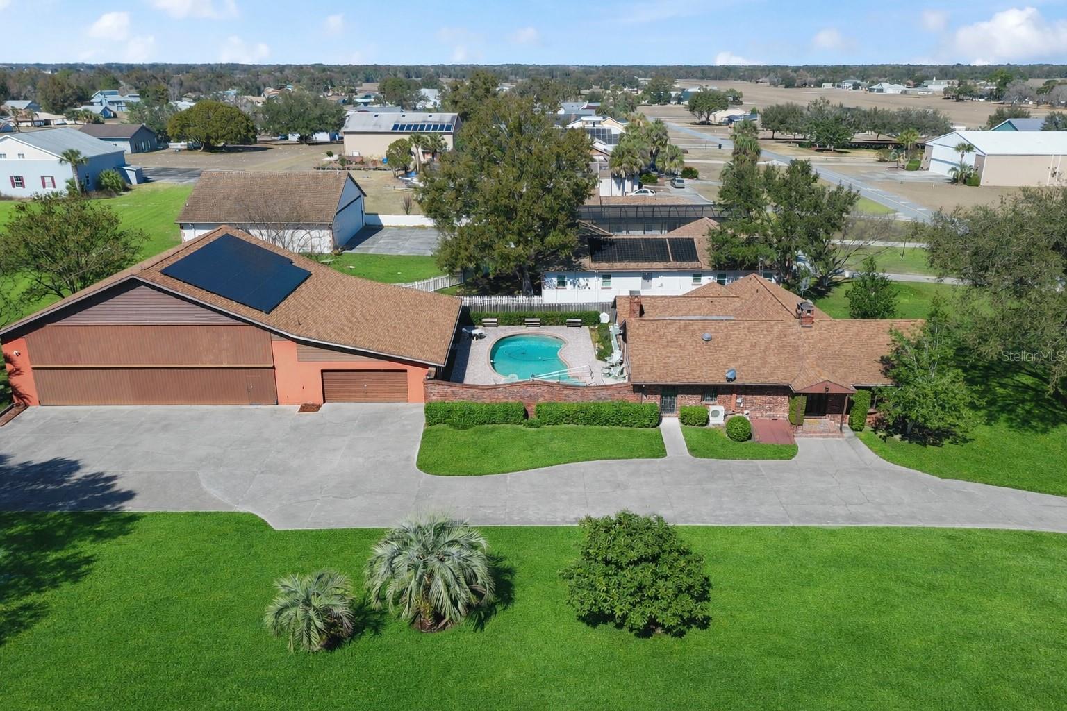 One or more photo(s) has been virtually staged. Welcome to a rare opportunity in the Leeward Air Ranch, a gated Central Florida airport community.  Warm and inviting 3/2 brick home with large hangar on 1.77 acres is offered only to licensed pilots who own an airplane!  Enjoy the view from your living room with wood burning fireplace and cathedral ceiling with exposed beams. Windows at the front and back of the home go all the way to the top for lots of natural light.  Wide plank, solid hardwood floors are beautiful and made to last.  See and feel the quality.  The primary suite is 20x20 with a fireplace and opens through French doors to the huge Florida room looking out to an in-ground saltwater pool. Paver decking leads you beyond the private courtyard to the 50x60 hangar.  With a door opening of 50x14'8” or higher, you can store your airplane and also fit an RV and/or boat.  There’s so much more!  Attached to the hangar are an over-sized 2 car garage and an apartment with full kitchen, full bath and laundry-- ideal for guests, extended family or pilot quarters.  Want to change your own oil?  There's a maintenance pit with water and power!  Need more storage? Check out the full basement! New shingle roof was installed on both the house and hangar in 2019.  Whole house solar panels installed in 2025 will keep the electric bill low. The lease will be pre-payed by the seller for the next 24 years!  Property is on well and septic-- no water or sewer bills!   Taxi from your home to the north/south runway, a reinforced and lighted grass strip 6200 x 165.  Many activities await the new owner such as fly-in's and weekly fly-out's with blue skies all year long.  Non-aviation activities include art, bingo, exercise, music events, hangar happy hours, motorcycle rides, etc.  Celebrate the holidays with your neighbors in our Red Barn Community Center.  Golf enthusiasts will love the beautiful 18 hole course nearby.  Low, low HOA fees, only $2930 year..  Don't wait, make this house your forever home.  Priced right so you can update to your style!