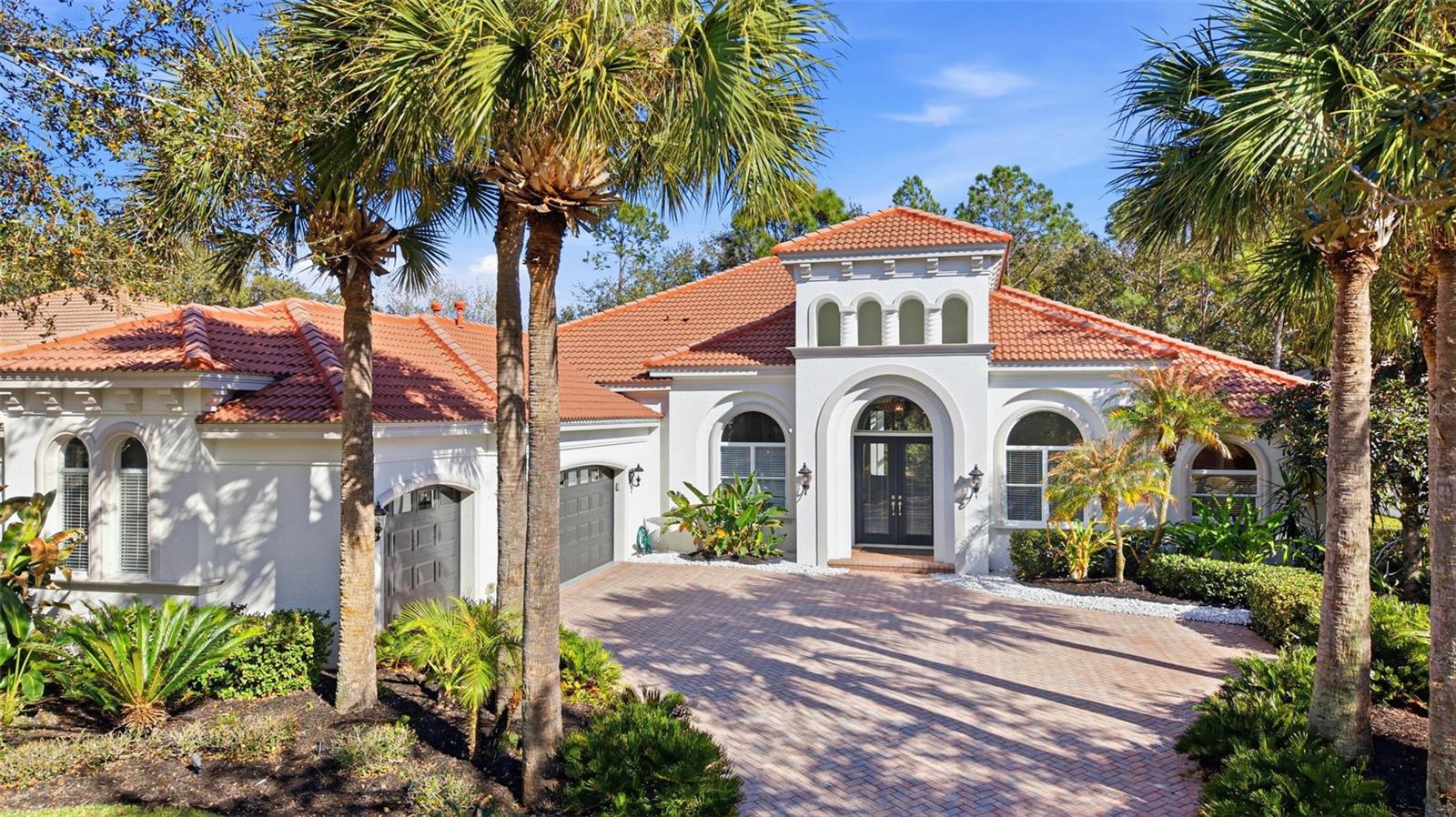 One or more photo(s) has been virtually staged. Located within the prestigious, gated community of Grand Hampton, this Mediterranean-inspired Taylor Woodrow residence at 20107 Oak Alley Drive offers 4 bedrooms, 4 bathrooms, a 3-car garage, and a private pool—an exceptional blend of architectural presence and elevated modern design. A sweeping paver driveway framed by Florida-friendly landscaping creates a striking approach. The signature elevated tower showcases arched openings, Solomonic columns, and architectural lighting that highlight its Mediterranean character. The covered entryway and double glass doors introduce bright interiors filled with natural light. Inside, arched windows illuminate the foyer, accented by tray ceilings with crown molding and Travertine tile flooring throughout the interior. Just off the entry, the formal dining room connects seamlessly to the main living areas. The dining space flows into the expansive family room, where oversized windows frame conservation views and the outdoor living area. A private office or flex space sits nearby. Down the hall, a full pool bath with a glass walk-in shower provides convenient exterior access. The primary suite is privately situated behind double doors and features tray ceilings with crown molding, recessed lighting, a custom inlay wall detail, expansive windows, private lanai access, and two walk-in closets. The primary ensuite bath includes a single extended vanity with dual sinks and granite countertops, a soaking tub, and a spacious glass walk-in shower. On the opposite wing, a quartz-appointed dry bar with wine refrigerator and upper and lower cabinetry enhances entertaining. The laundry room offers a stackable washer and dryer, utility sink, folding station, and ample cabinet storage. Bedrooms two and three share a Jack-and-Jill bath with dual sinks and modern finishes. The fully updated kitchen presents a clean, elevated design with quartz countertops, glass inlay cabinetry, apron-front sink, oversized island with seating, built-in pull-out trash bin, and recessed lighting. Premium Monogram stainless steel appliances include a gas range with hood, built-in microwave/convection oven, refrigerator, and integrated shelving. Two pantry closets—one a dedicated butler’s pantry—provide excellent storage. The adjacent dinette overlooks the pool and flows into the living area with sliding glass doors and tray ceilings. An expansive bonus/flex room offers space for a media room, game room, or secondary living area. Just off this space, the fourth bedroom and full bath create a private guest suite. The outdoor living area features an extended lanai finished in travertine pavers, two covered seating areas, and a screened pool with blue tile accents and ambient lighting. The outdoor kitchen is equipped with a built-in gas grill, cooktop, refrigerator, sink, and pull-out trash bin, all set against peaceful conservation views. The 3-car garage includes epoxy-coated floors, MyQ app-controlled openers, and two large storage areas, one with a workbench. Notable updates include HVAC systems (2020 & 2021), Water Heater (2024), and Pool Pump (2026). Grand Hampton offers 24-hour gated security and resort-style amenities including a clubhouse, fitness center, lagoon and lap pools, tennis and basketball courts. Conveniently located near I-75 and I-275, AdventHealth, Pasco-Hernando State College, AdventHealth Center Ice, The Shops at Wiregrass, and Tampa Premium Outlets. Schedule your private showing today.