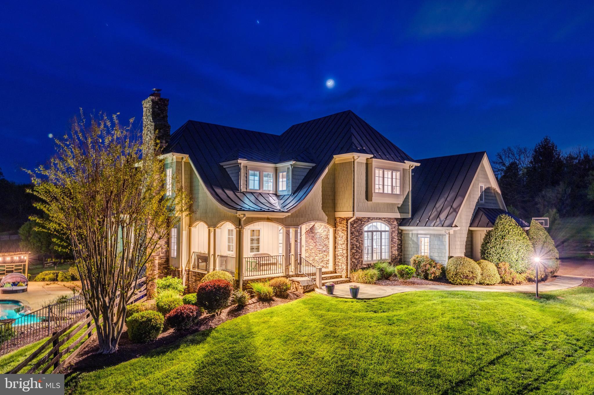 Welcome to Skyfall, a custom-built modern farmhouse thoughtfully designed with the finest materials, exuding sophisticated luxury on 9.08 meticulously fenced acres secured by private electric-gate access. Nestled on prestigious Peale Lane—a secluded enclave celebrated for estate-quality homes amid Loudoun County’s picturesque wine country—Skyfall offers exceptional privacy, yet is mere minutes from vibrant downtown Leesburg. Crafted with impeccable attention to detail, the home's striking entry features imported black French steel doors beneath a dazzling Schonbek German crystal chandelier, accented by tray ceilings and crown molding throughout the main level. Durable Hardi-plank siding, a sleek full metal roof, and new Carrier HVAC systems with UV technology underscore the superior quality of construction. The luxurious main-level primary suite includes dual walk-in closets, French steel doors, and a cozy sitting area with a Jotul wood stove surrounded by marble. Its opulent ensuite bath features reclaimed barn doors, cathedral-arched windows, an oversized Kohler soaking tub, Toto Japanese toilet, dual Indian marble vanities, and frameless rainfall shower. Two chic powder rooms—including one concealed within the laundry—ensure convenience. Ascend the dramatic waterfall staircase to three spacious bedrooms, each with generous walk-in closets. One bedroom has a private ensuite bath with marble vanity; the other two share a Jack-and-Jill bathroom with dual Carrera marble vanities, clawfoot tub, and seamless glass shower. A charming reading nook completes the upper level. The gourmet kitchen impresses with expansive floor-to-ceiling cabinetry, waterfall quartz island with cabinetry on both sides and integrated power, WiFi-enabled Thermador appliances including discreetly integrated fridge, freezer, dishwasher, wine fridge,  6-burner range with griddle, twin ovens and integrated Chef's hood.. Under-cabinet lighting, hidden outlets, and a trough sink with dual faucets enhance functionality. An adjacent hidden pantry mirrors kitchen finishes with quartz counters and open English oak shelves, and handmade hickory barn door entrance. The expansive family room features soaring cathedral ceilings, exposed wood beams, rustic stone fireplace insert, built-in English oak workspace, and access to the wraparound porch. A formal dining room, illuminated by a statement fixture, is perfect for entertaining. The finished lower level is an entertainer’s paradise, highlighted by a reclaimed Virginia barn wood bar with Indian marble, dishwasher, EuroCave wine fridges, beer fridge, and sink. A stacked stone fireplace with Jotul stove warms the rec room, while a hidden theater/music room lies behind a custom bookcase. A guest suite with reclaimed wood vanity and full bath, fitness room, workshop, and ample storage offer additional comfort, all with direct access to the pool deck. The outdoor haven centers around a stunning 30,000-gallon PebbleTech gunite pool, tanning ledge, 8–10-person spa, and impressive 11.5-ft deep end, that slopes to a swallower end.. Exterior amenities include a Trex deck, flagstone patio with Jotul fire pit, and stone-enhanced pool deck. Custom artisan electric gates by Aurora Services on Virginia bluestone columns feature AES PRO smart-device control. Equestrian facilities include a pristine 4-stall barn with new metal roof, hot/cold water, tack room, hayloft, and adjoining 7-acre fenced paddock. Facing nearly due south, Skyfall feels secluded and serene yet is conveniently situated only minutes from Dulles Airport and within easy driving distance of Washington, DC. Located just 4.6 miles from historic Leesburg with quick access to Route 15, the Greenway, over 50 wineries and breweries, and scenic trails including the Appalachian Trail, Skyfall represents a rare opportunity to experience refined craftsmanship and luxurious comfort in Northern Virginia’s most desirable countryside setting.