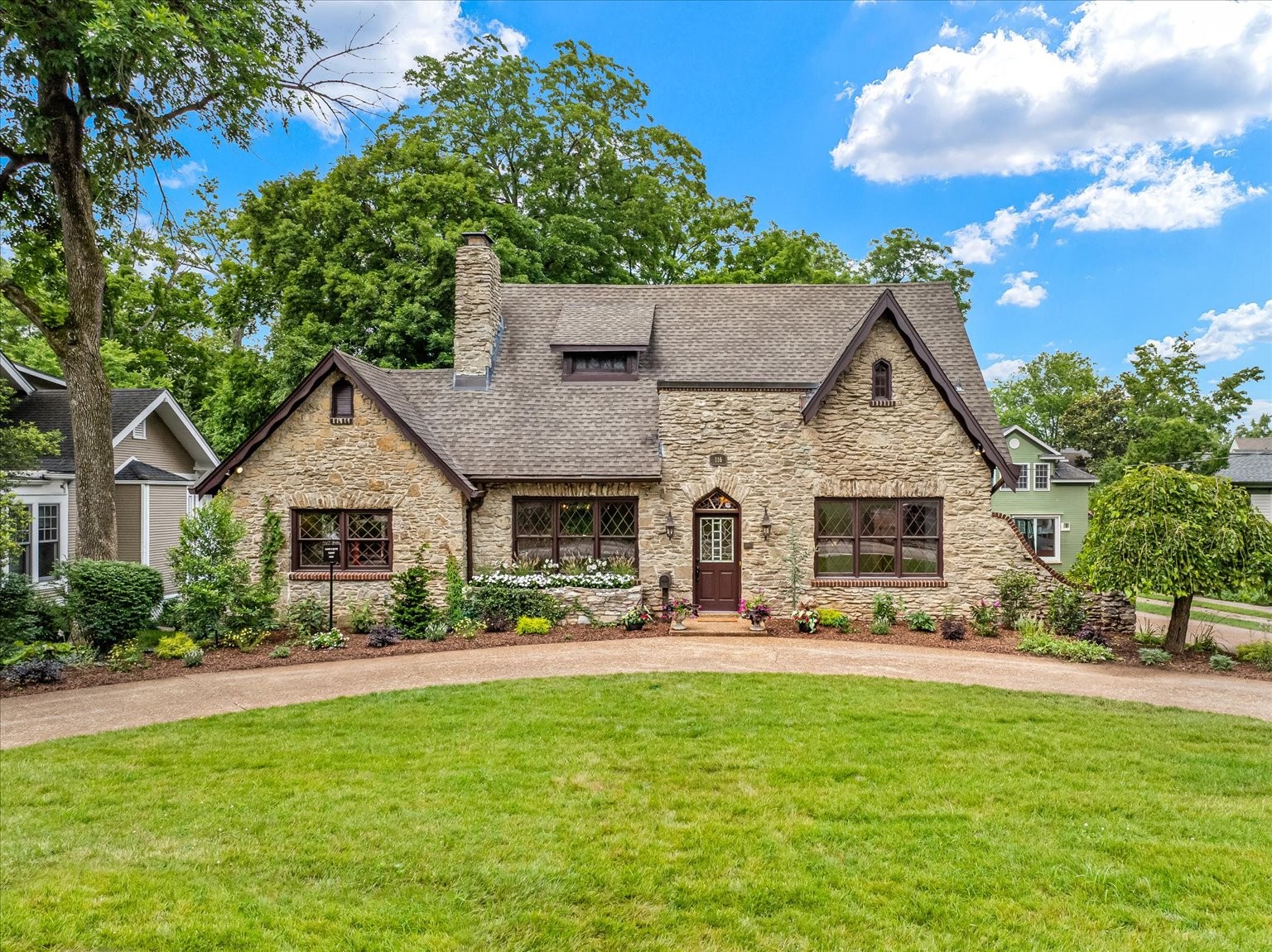 Nestled in the heart of Franklin’s prestigious Lewisburg Avenue Historic District, this stunning 1930 English Stone Tudor is a rare architectural gem listed on the National Register of Historic Places. Located on one of Franklin’s most iconic and picturesque streets, it’s just a short 10-minute walk to America’s Favorite Main Street. Thoughtfully reimagined for modern living, the open-concept main level blends timeless elegance with contemporary comfort. A dual-sided gas and wood-burning fireplace separates the formal living and dining rooms, while the dining area is crowned by a vaulted ceiling with exposed beams and candelabra chandeliers. At the heart of the home lies a brand-new chef’s kitchen that seamlessly combines vintage charm with state-of-the-art amenities. Features include a generous island ideal for entertaining, panel-ready appliances, an appliance garage, an Ilve gas range, and a dual-zone wine and beverage fridge—making this kitchen as functional as it is beautiful. Architectural details abound: a steeply pitched roofline, stone chimney, Tudor-inspired diamond-paned windows, original staircase, and exquisite stained-glass accents. Richly finished hardwood floors, natural stone, quartzite, marble, and unlacquered brass fixtures lend a sense of timeless luxury. The serene main-level primary suite offers a true retreat, complete with custom built-ins, period lighting & bespoke wallpaper. The spa-like en-suite bath features heated floors, marble surfaces, and an oversized shower. The walk-in closet includes a built-in vanity for added charm and functionality. Additional amenities include an interior/exterior built-in speaker system, a whimsical first-floor laundry room with brand-new appliances and a spacious basement offering plenty of storage or potential for expansion. Outside, relax in the peaceful, park-like backyard sanctuary, perfect for entertaining or enjoying quiet moments. This one-of-a-kind historic treasure is truly the home of your dreams.
