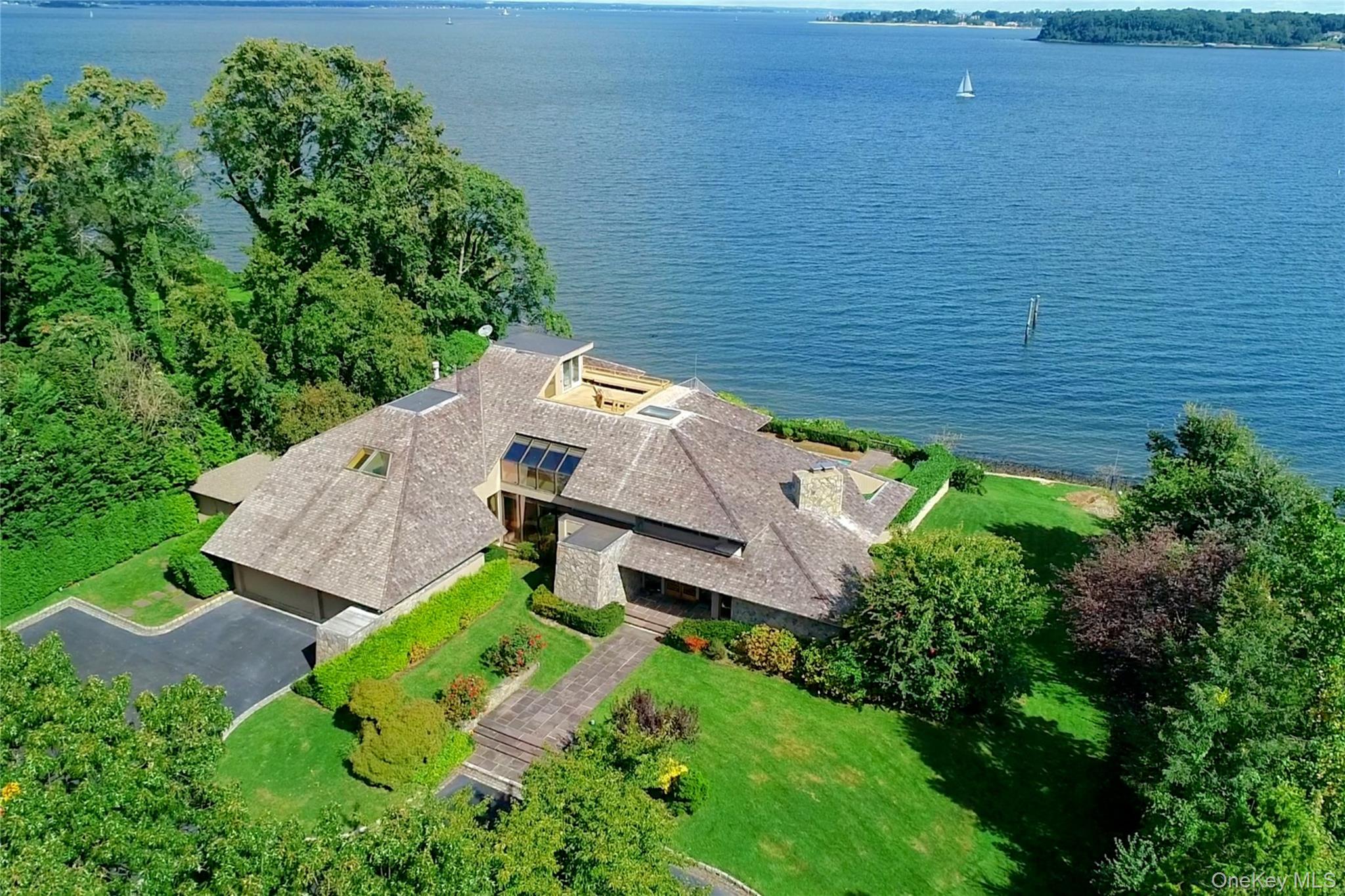 A Luxe Waterfront Estate of Privacy & PrestigeAt the end of a discreet cul-de-sac in Kings Point sits a residence of rare distinction. 15 Gatsby Lane is more than a waterfront home—it's a private luxury estate, elevated high above the Long Island Sound and wrapped in seclusion, grandeur, and breathtaking panoramic views.Set on over an acre of prime Gold Coast land, the property commands attention from the moment of arrival. Mature landscaping, generous setbacks, and its elevated positioning ensure total privacy, while the residence opens dramatically toward the water with sweeping walls of glass, soaring ceilings, and a collection of balconies and terraces designed for life lived above the shoreline.Inside, 6,300+ square feet unfold with quiet sophistication. Every space feels intentional—layered with natural light, volume, and curated sightlines that celebrate the Sound at every turn. Formal rooms flow with elegance; casual spaces offer relaxed luxury; and each transition reveals another shimmering water view.The primary suite is a sanctuary of true indulgence—privately set, with dual spa baths, a serene lounge, and direct access to outdoor terraces, including a spectacular rooftop deck that elevates sunrise, sunset, and starlit evenings into unforgettable moments.With five bedrooms, seven baths (6 full, 1 half), and flexible living spaces for hosting, or unwinding, the home supports both intimate daily living and elevated entertaining. The expansive grounds offer endless potential to create a resort-level outdoor environment—pool, gardens, lounge terraces—all enhanced by the estate’s commanding waterfront perch.In a community defined by exclusivity, 15 Gatsby Lane stands apart—a rare offering where privacy, luxury, and an exceptional waterfront setting converge into one extraordinary Kings Point estate.