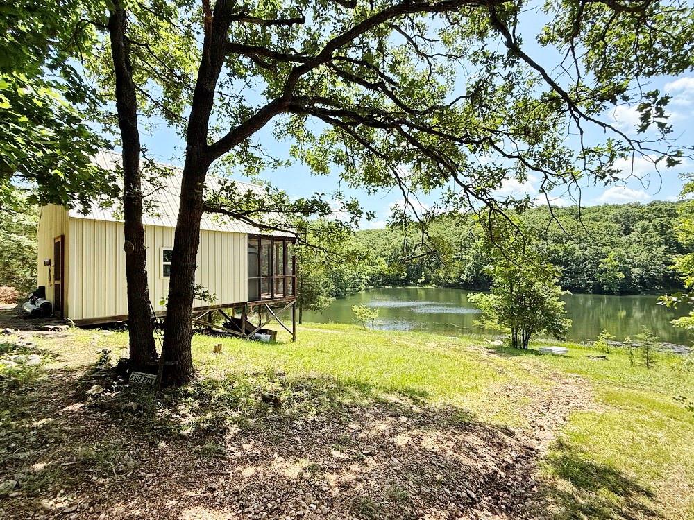 Perfect Combination of Seclusion, Recreation, and Relaxation – located southwest of Collins, Missouri is this 80-acre wooded tract of recreational property that truly gets you off the grid. The land is accessed down a ¾ mile easement and arrives at the property in front of an A-frame cabin that overlooks the 2.5-acre lake. The cabin is just over 50’ from the lake edge where you can view sunrises, wildlife, and just slow down life from the serene view off the 8’x16’ screened-in porch.  The enclosed portion of the cabin is 16’x16’ plus an 8’x14’ loft area, giving a total living space of 384 sq ft + 128 sq ft on the screened-in porch. There is no water or electricity at the cabin, so the seller uses batteries and brings his own water to the cabin to use in the outdoor shower space.  Just east of the cabin is the “fanciest outhouse” that you will ever see (no, really, it is)! The edge of the lake shore in front of the cabin has been cleared, making the perfect launch point for boats and canoes.  Imagine the hours you could spend fishing and relaxing on this lake. This property also features ~800’ of frontage with Brush Creek providing additional fishing and recreational opportunities. A decent trail system is in place which accesses the NE corner of the property, the Brush Creek frontage, and a longer loop-trail going east, then south of the lake to access a high oak flat on top of the hill. Just try and hear any road noise from this location! This property can also be used as a jumping point to Truman Lake (20 minutes), Pomme de Terre Lake (20 minutes) or Stockton Lake (15 minutes). All these lakes provide incredible fishing, boating, hunting, and many other recreational opportunities. Call today to find out what a true off-grid experience looks like. Let’s go take a tour!
