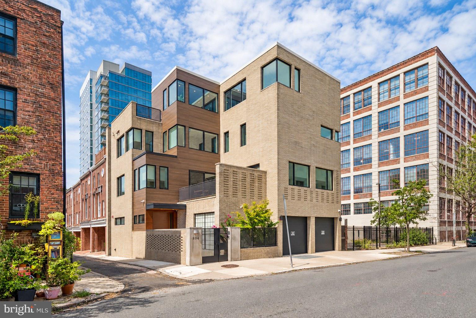 The one you couldn’t have asked for until you knew it already existed. One house. One site. One design. A stunning corner residence stretching four stories into the air. Cream masonry. Warm wood. Steel. Glass. Staggered planes, private terraces, unexpected expanses of glazing. Restrained yet remarkable. An illuminated stone pier, 254 etched into it. Private gate. Protected entry court. The home rising quietly yet boldly behind. Inside, the first reveal: an entry gallery draws you in. Heated slate underfoot. Light cascading from above. A sculptural steel staircase with open oak treads, cable and frameless glass: a luminous column connecting all levels. Up one: the heart of the home. The living room, where expanses of glass fold away to a substantial terrace. Corner fireplace. Open sky. Light from every direction. The house begins to unfurl. Expansive, radiant, yet exquisitely private. Breakfast area. A stunning Wolf-and-Sub-Zero kitchen. Walk-in pantry. Powder room. Formal dining room with fully equipped bar, the first of three throughout the residence. Up a level, another reveal. Three guest bedrooms with walk-in storage. One en-suite bath; two share a Jack-and-Jill bath with dual sinks, dual showerheads and separate water closet. A guest lounge with its own laundry: watch television, work, unwind, spend an entire day without leaving the floor. Not simply somewhere for guests to sleep. A place for them to live. The fourth level: this belongs entirely to you. A light-filled landing precedes a three-workstation office. Then, the owner’s sanctuary. A sleeping area and lounge connected by a double-sided television partition. Outside, a private terrace with a fire feature and panoramic east-and-west views. Storage that seemingly disappears into the walls. Double dressing rooms precede the owner’s bath. A suspended, wall-to-wall vanity beneath an overhead skylight. Light spills everywhere, creating an ethereal sense of scale and calm. Expansive shower. Jetted soaking tub. Impossibly restrained finishes. The whole level, total tranquility. A private enclave unto itself. Descend by elevator to the lower level. A private fitness club. Substantial, exceptionally equipped. Rubber flooring underfoot. A dramatic two-story climbing wall with electronic safety system. The look and capability of a professional training facility. Dedicated television and beverage station. Adjacent: a home theater with projector, motorized screen and inset speakers. A service kitchen with exotic cabinetry and integrated dishwasher. Full bath just steps away. All of it below grade. A hidden world you’d never know existed. Behind a door: the technology center. Crestron automation. Lutron programmable lighting and motorized shades. Tunable-white illumination. Five-zone HVAC. Hardwired UniFi networking. Security and leak detection. Radiant heat across multiple levels. Backup generator. Intelligence everywhere, technology tucked beyond sight. And then, back to where we entered. Behind the serene entry gallery, a household-management level has been hiding in plain sight. A private housekeeper’s suite with en-suite bath. Laundry and household-management room with cabinetry, sink, extensive counter space, built-in workstation, concealed ironing board and retractable drying rack. Zoned fragrance. Cedar closet. Heated floors. A second point of entry from the two-car garage via a dedicated vestibule with benches and storage. Close the doors and nearly all of it disappears. Open them, and everything is exactly where it should be. Present when you need it. Invisible when you don’t. At night, 254 metamorphoses. Cream masonry glows. Warm light pours through glass. Four stories rise and recede in a rhythm of illuminated planes and terraces. By day, the house collects light. At night, it gives it back. A hallmark of the Fitler Square skyline.