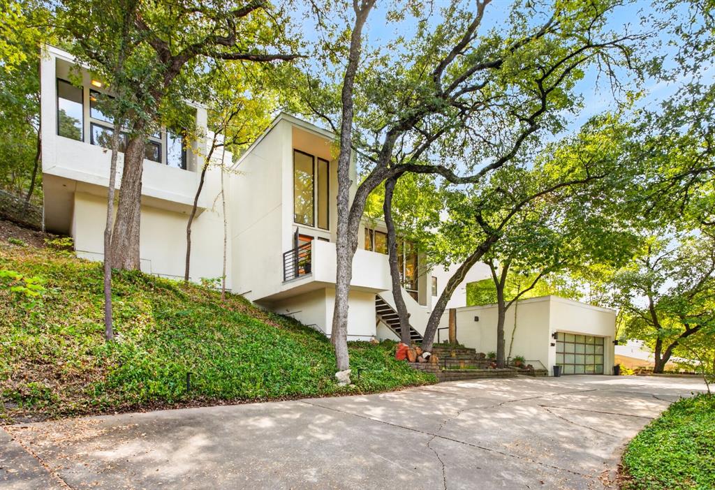 Stunning and iconic cubist architecture in the heart of Tanglewood!  Nestled in the treetops with 3 levels, this home offers incredible views of the Fort Worth skyline when the trees shed their leaves.  Gorgeous windows and a minimalist design create a welcoming appeal!  Featuring 3 living areas, 2  dining areas, 4 bedrooms, 2 full bathrooms and 2 half baths.  Part of this home's appeal is that every level offers something unique and special.  The first level has a built in Murphy bed, its own half bath, a private patio, and a built-in desk making it a perfect space for guests or a home office.  The main level has a formal living area with soaring ceilings, floor to ceiling windows that overlook the front of the home and great custom built ins.  The kitchen featuring updated cabinetry and stainless appliances, your breakfast room with a sliding door onto the patio and your formal dining area—which is perfect for hosting intimate dinners—are also on this level with views to the backyard and patio!  The gorgeous primary ensuite feels like a spa, featuring floor-to-ceiling windows and a sliding glass door opening onto your private balcony. The large windows in your primary bath that look out into your own private nature retreat are so peaceful and you have a generous sized walk in closet  Two additional bedrooms, a full bath, a second living area with a wet bar and a music room complete the home's third level.  The vertical design of this home is made even more special by the built in elevator that gives a homeowner access to all three floors.  Situated on a third of an acre, this home has an incredible amount of trees and natural landscape and the owners have enjoyed all of the decking and pergolas perched up on the hill behind this home.  Enjoy an evening with friends in your own private oasis. This home offers a lifestyle and truly feels organic, with spaces inside and out for entertaining guests and hosting family and friends!