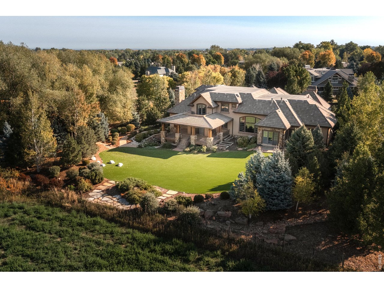 Set on 1.16 private acres at the end of a quiet cul-de-sac in Boulder's sought-after White Hawk Ranch neighborhood, 8925 Mountain View Lane is a 12,339 square foot estate offering 8 bedrooms and 11 bathrooms across three finished levels, with sweeping mountain views and easy access to Boulder, Louisville, Lafayette, Waneka Lake, area golf, regional trails, and Boulder Valley schools. A stucco and Telluride stone exterior, arched glass entry doors, and a gated courtyard introduce a home defined by soaring ceilings, exposed beams, substantial millwork, iron detailing, and fireplaces throughout. The living room pairs mountain views with a fireplace, and the dining room opens to the courtyard for indoor-outdoor entertaining. The kitchen features custom cabinetry, poured concrete countertops, an oversized island with prep sink, and a walk-in pantry, flowing into an informal dining area and a gathering room with exposed beams, built-ins, and a desk nook. The main-level primary suite includes a fireplace, sitting area, walk-in closet, and private patio access, while a fireplace office with floor-to-ceiling shelving serves as a private library. Upstairs, a second primary suite offers a private balcony, walk-in closet, and mountain views, alongside two more en-suite bedrooms and a second laundry room. The lower level is a full height walk-out level with substantial natural light and functional living spaces, including four additional en-suite bedrooms, a recreation room with a stone fireplace and curved bar, a movie theater, and a second kitchen setup. Outdoor living includes a circular drive and motor court, a Cumaru hardwood deck, turf, and multiple balconies and patios. An elevator connects all three levels, with a mudroom, two laundry rooms, smart-home controls, radiant-floor heating, and seven garage bays. This Boulder luxury home offers privacy, space, and mountain views for everyday living and entertaining alike.